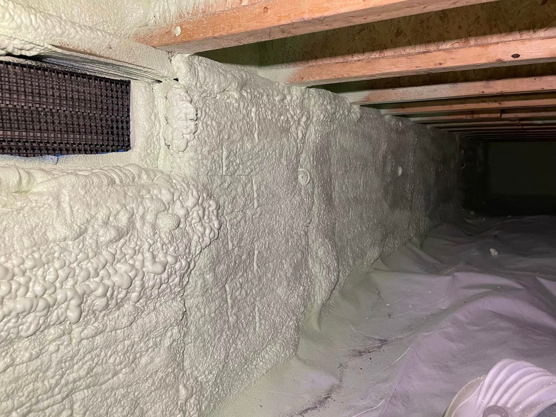 Foam-insulated crawl space with wooden beams and a vent opening along the wall