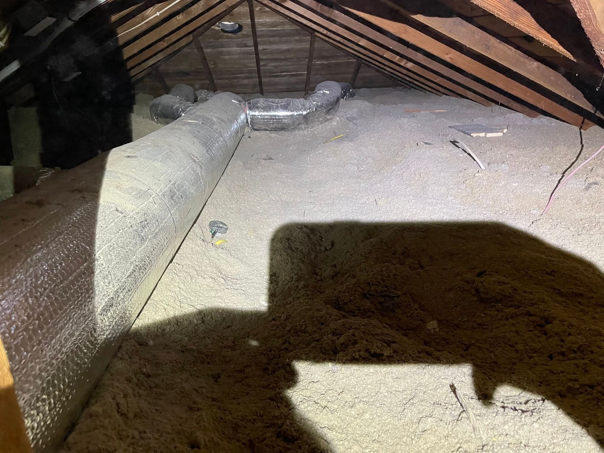 Insulated attic floor with exposed rafters and a large shadow cast across the surface