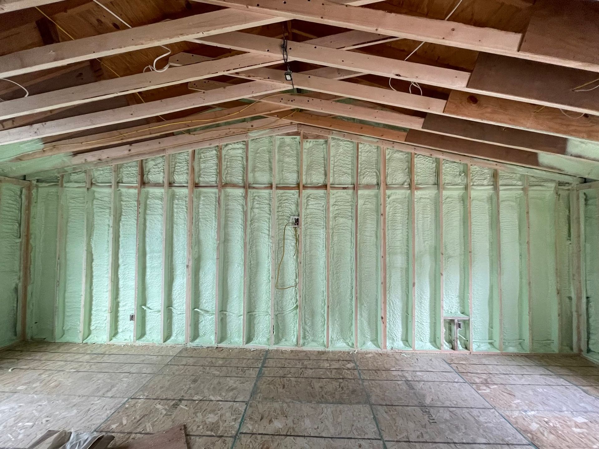 Empty unfinished room with exposed wooden rafters, insulated green walls, and a bare floor