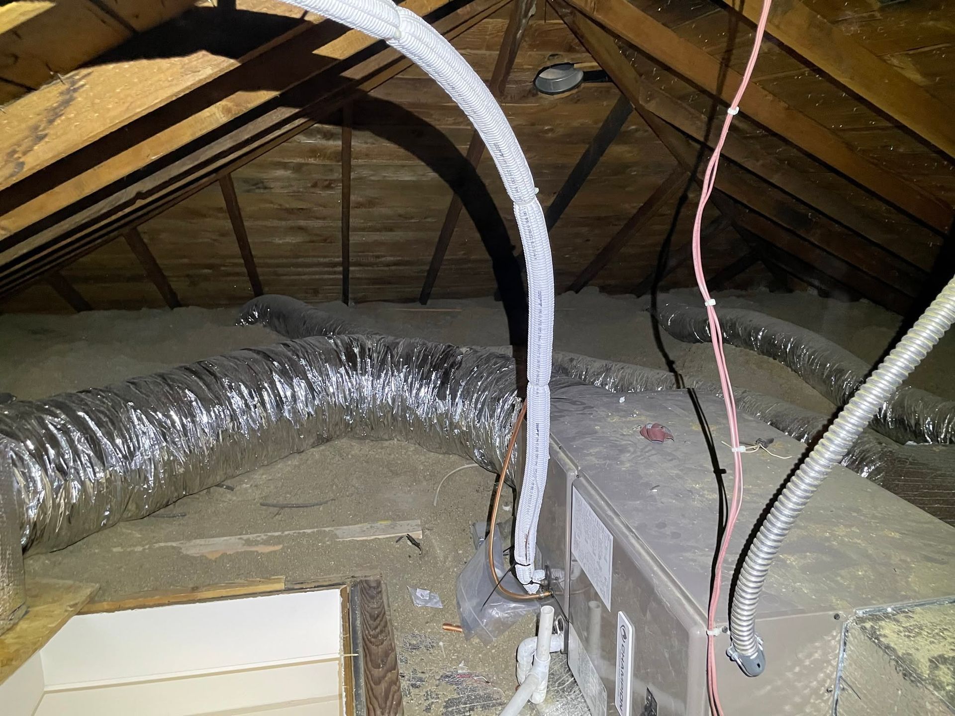 Attic with exposed insulation, ductwork, and electrical wiring beneath the roof rafters