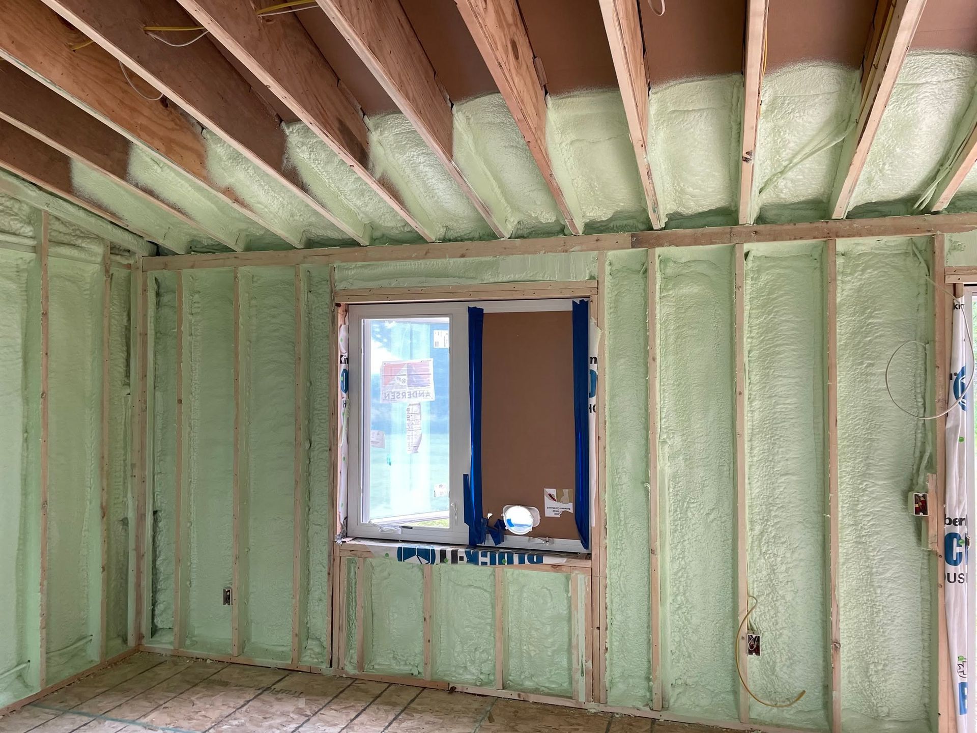 Interior wall under renovation with green insulation, exposed ceiling beams, and a window opening