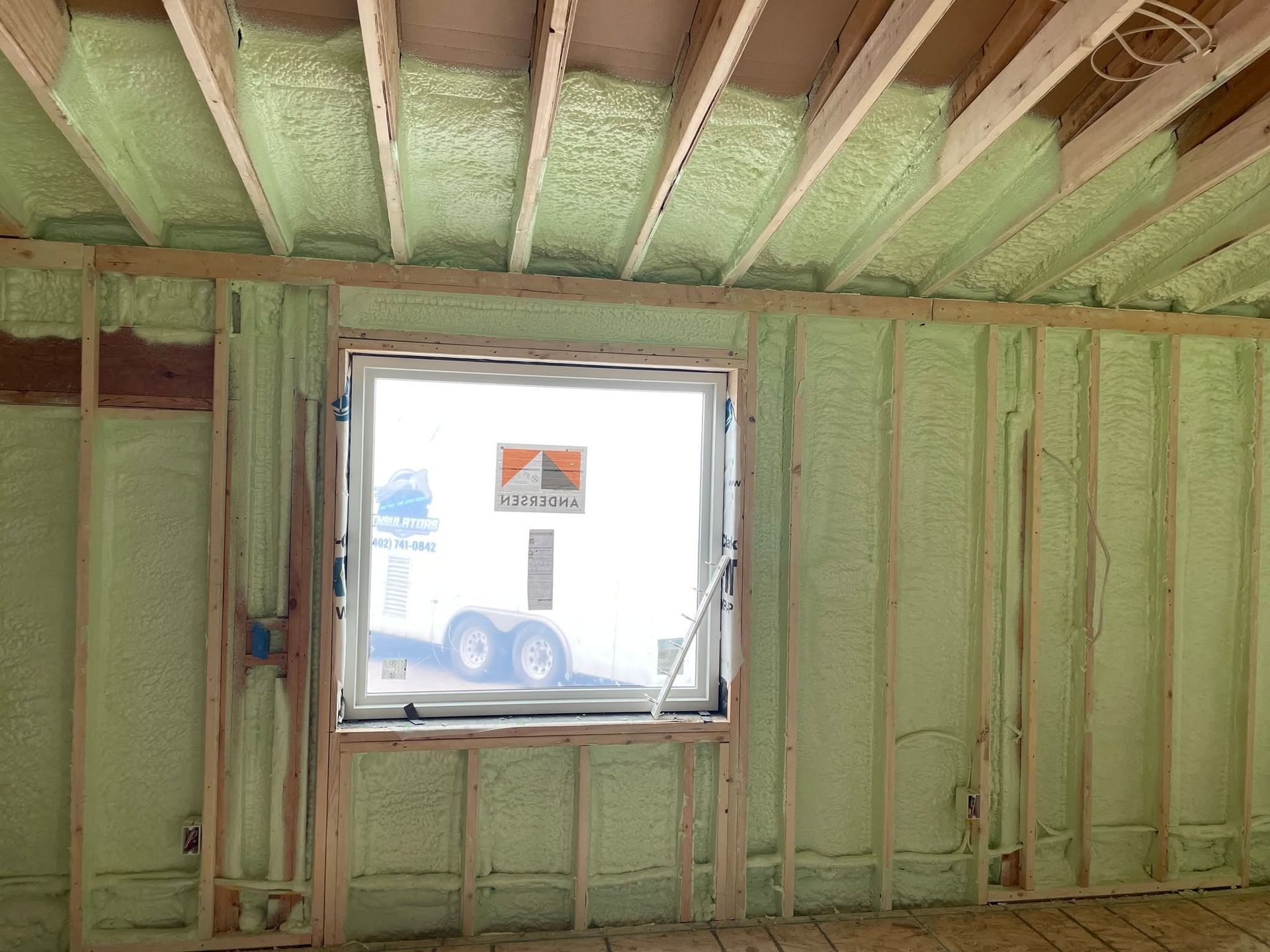 Insulated room interior with exposed ceiling beams and a window opening to a trailer outside.