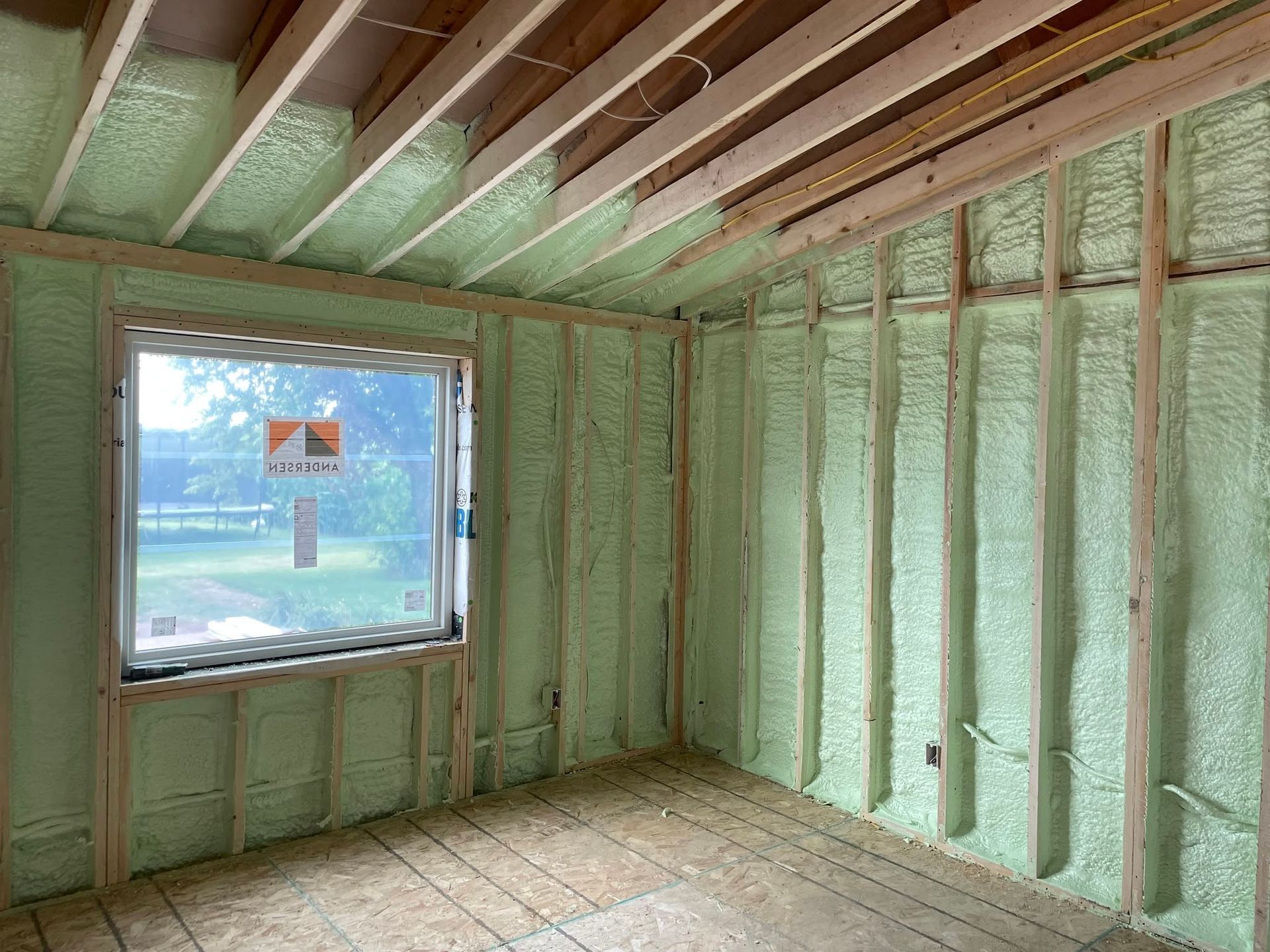 Interior of a room under construction with green spray insulation on walls and exposed ceiling joists