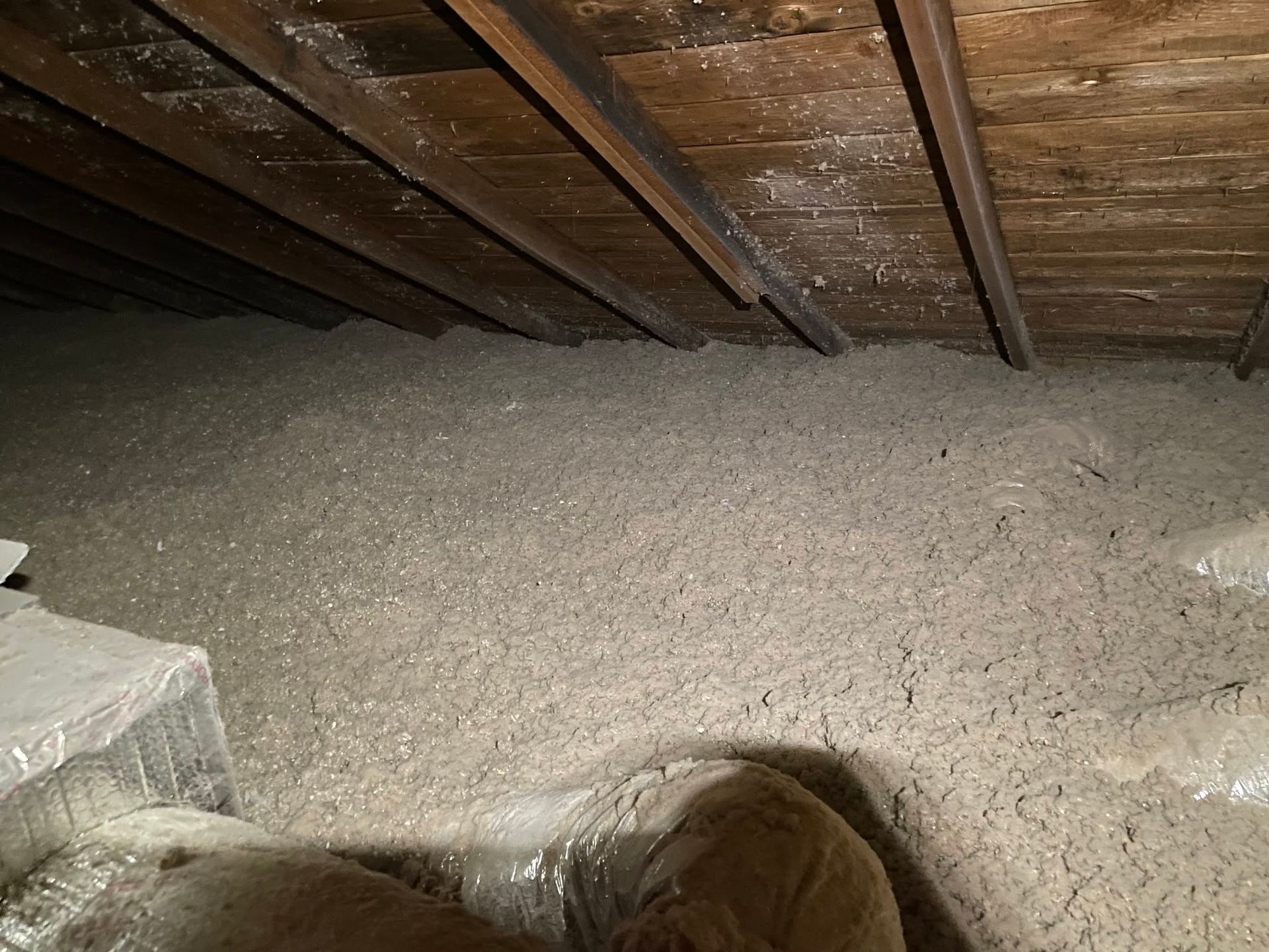Attic filled with loose insulation under exposed wooden rafters.