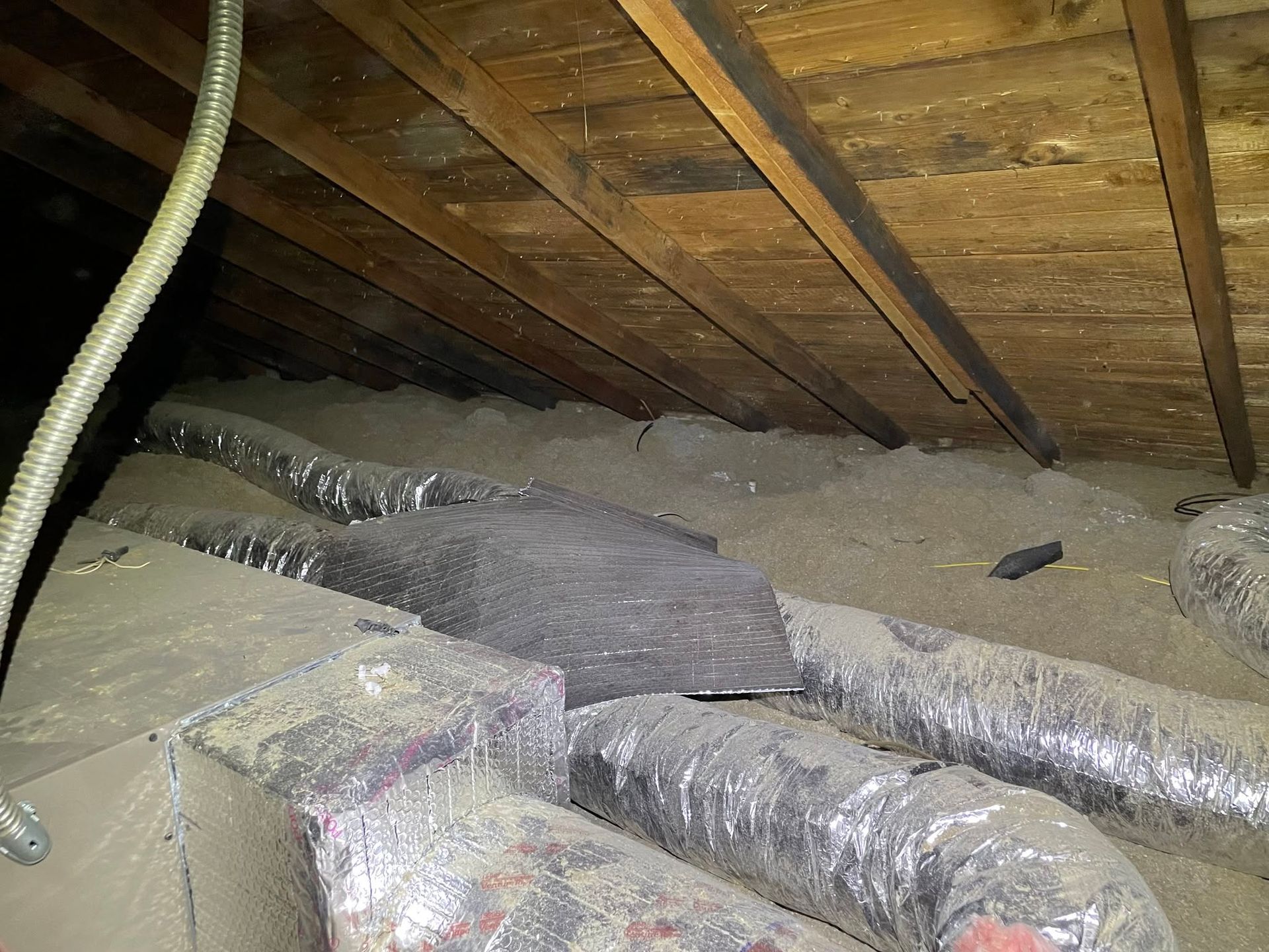 Attic crawlspace with exposed wooden rafters and insulated ducts running across the floor