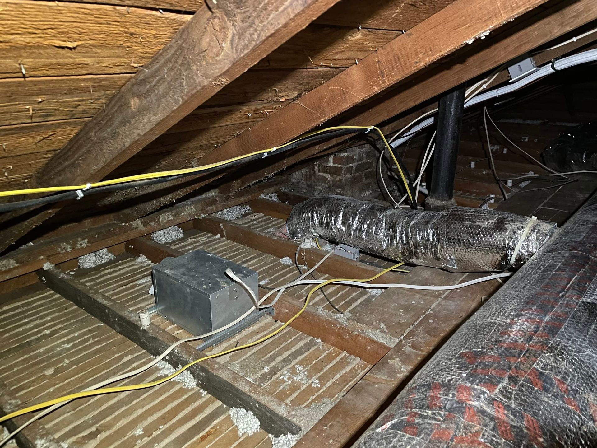 Attic crawlspace with exposed insulation, wiring, and wooden beams under a sloped roof