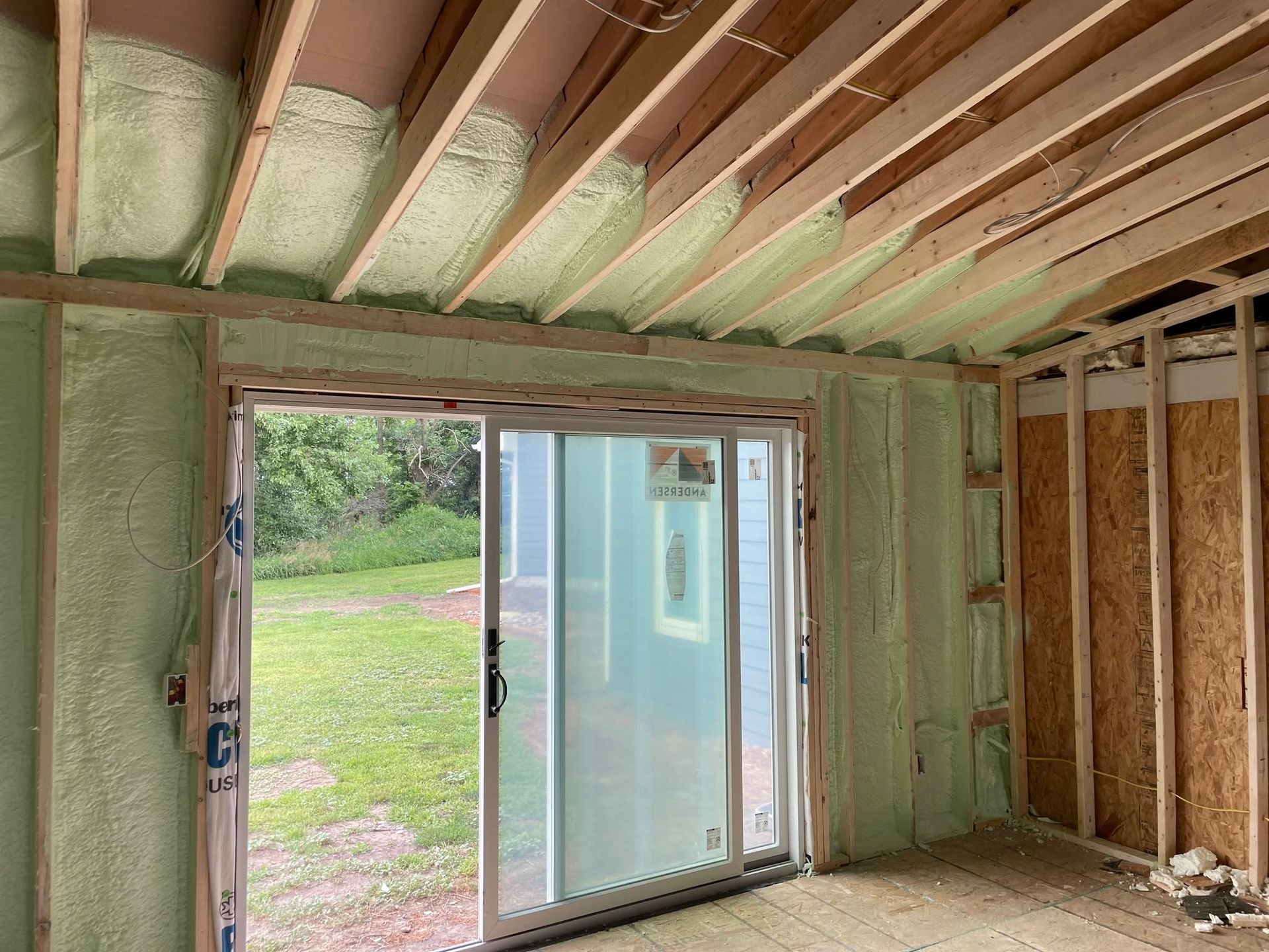 Insulated unfinished room with exposed ceiling joists and a sliding glass door opening to a grassy yard