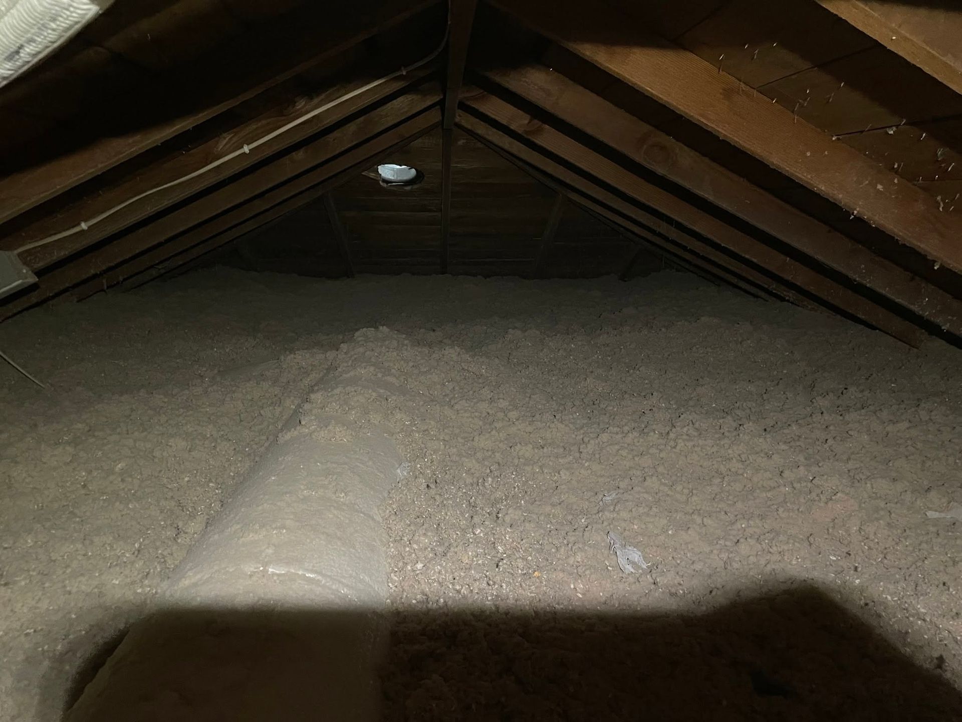 Insulated attic with exposed wooden rafters and a bright light fixture near the center.