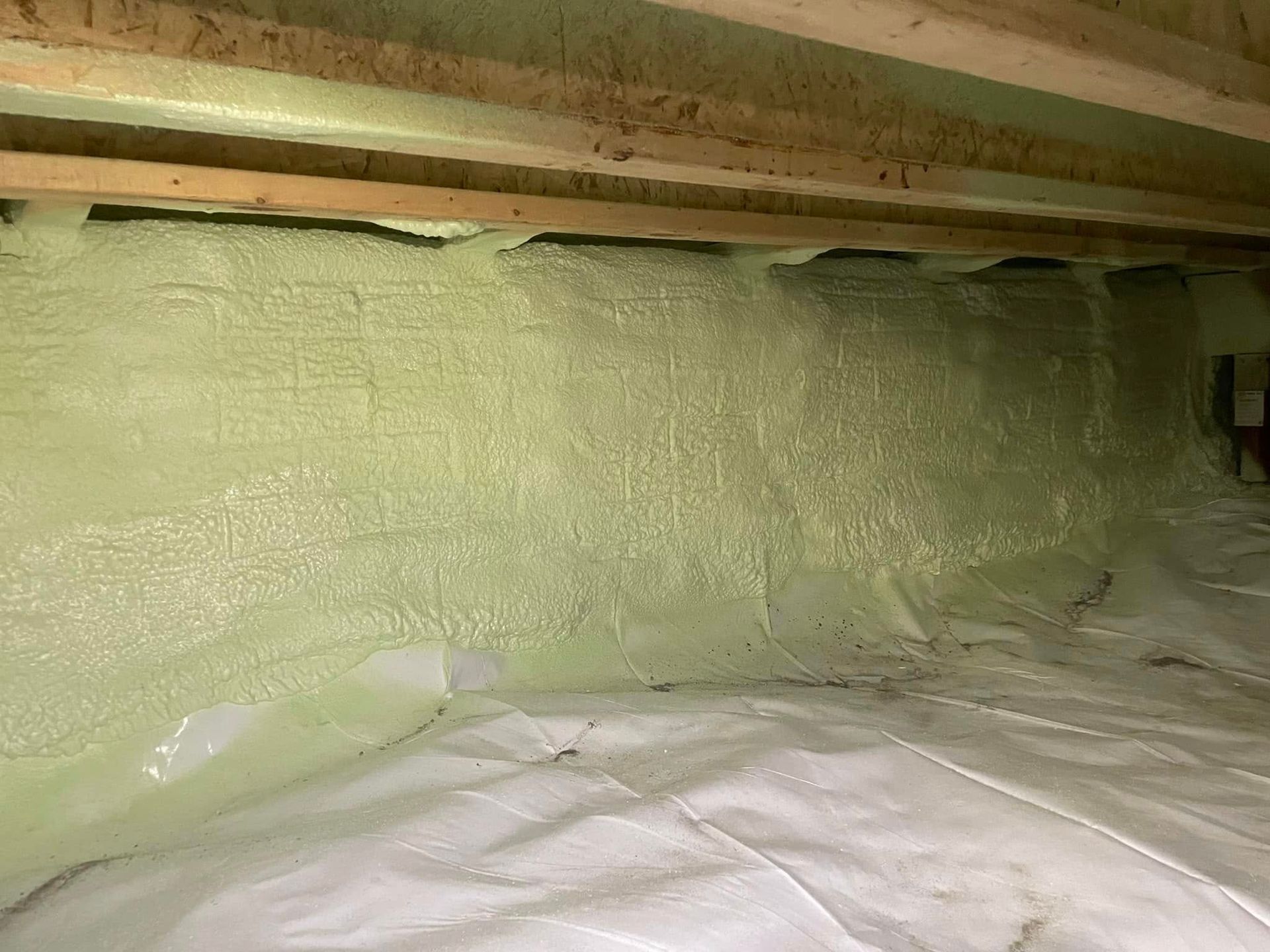 Insulated crawl space with green spray foam on wall and white plastic sheeting on the floor