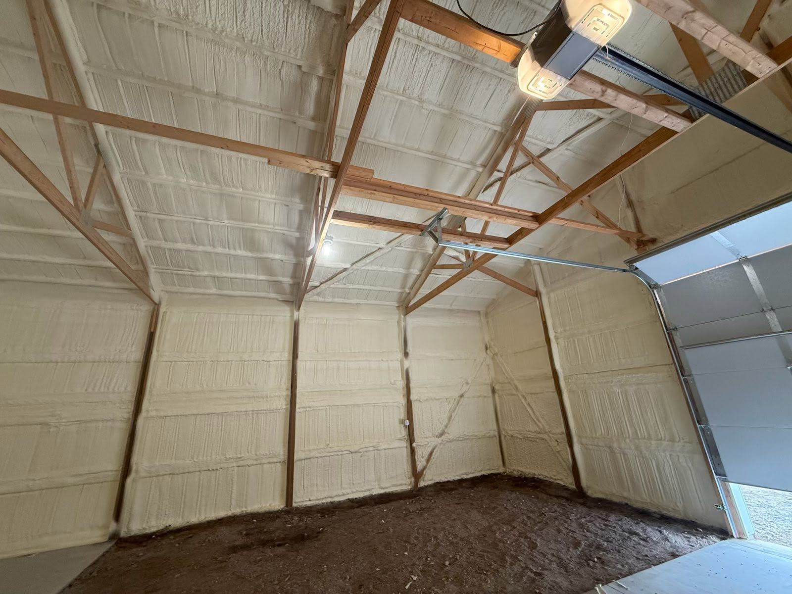 Empty insulated barn interior with exposed wooden rafters and dirt floor