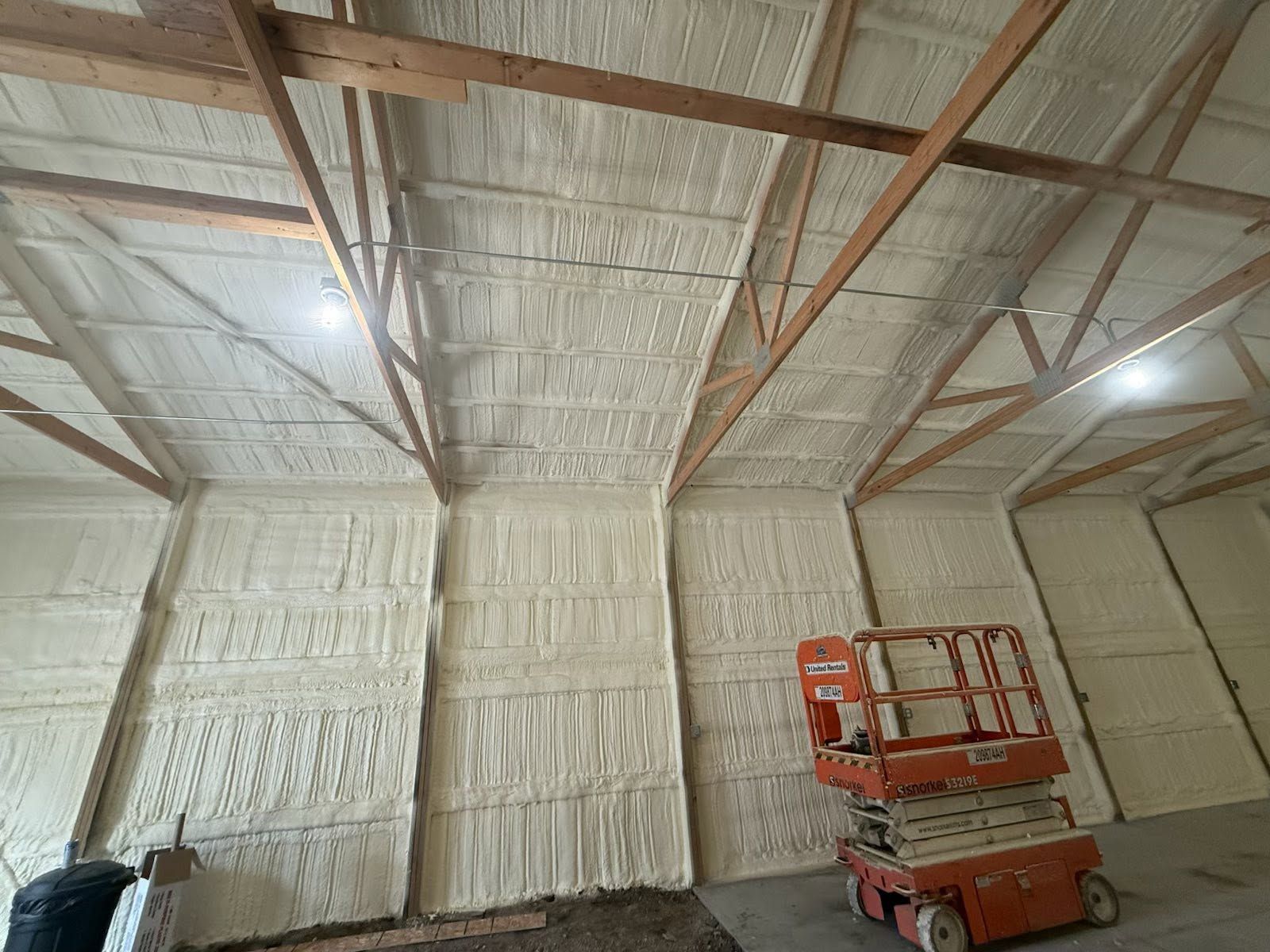 Insulated warehouse interior with exposed beams and a red scissor lift on the right