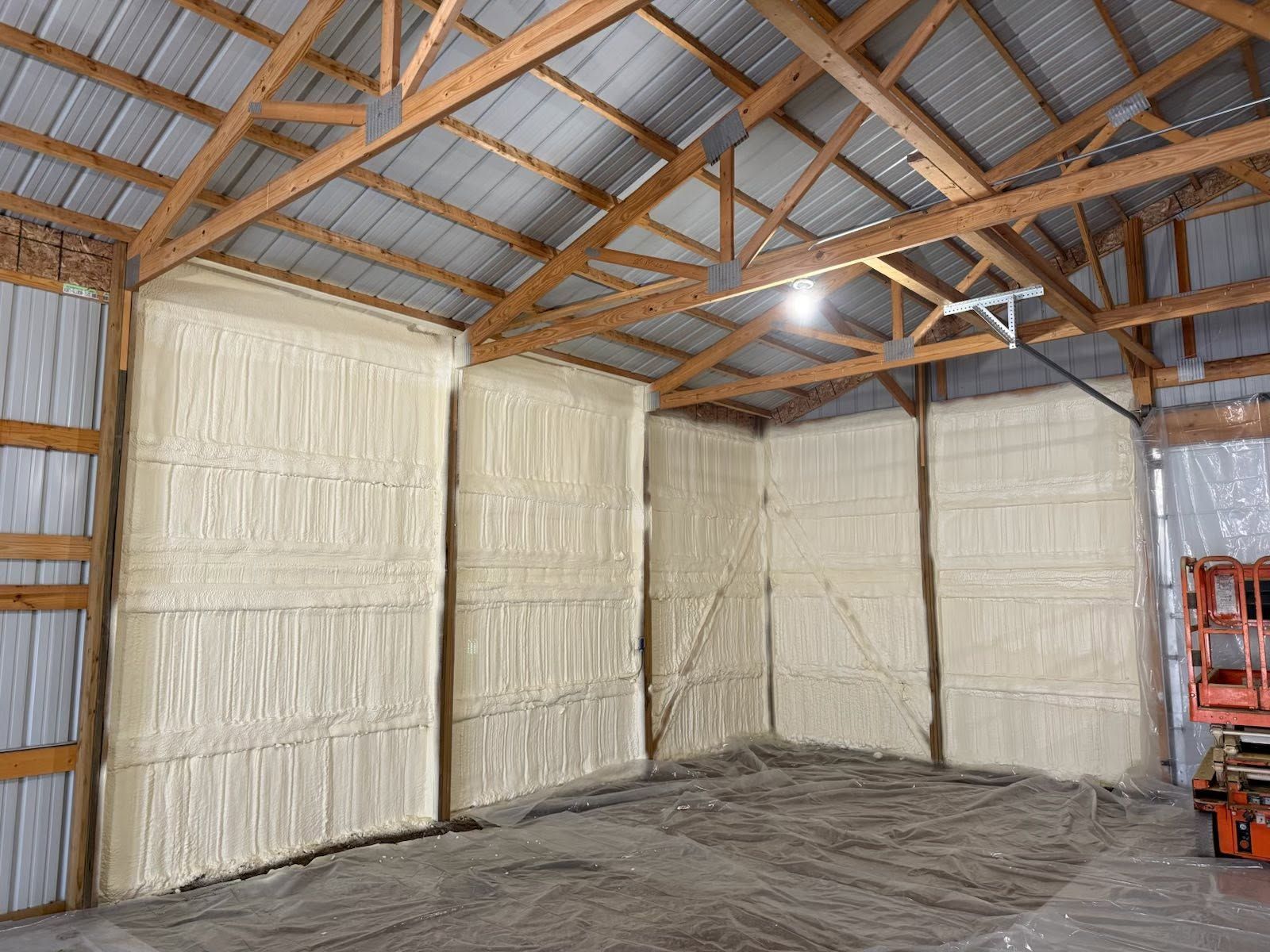 Insulated barn interior with wooden beams, white wall panels, and a concrete floor.