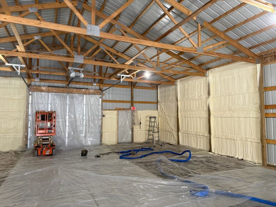 Insulated warehouse interior with exposed trusses, plastic-covered walls, lift, and hoses on the floor