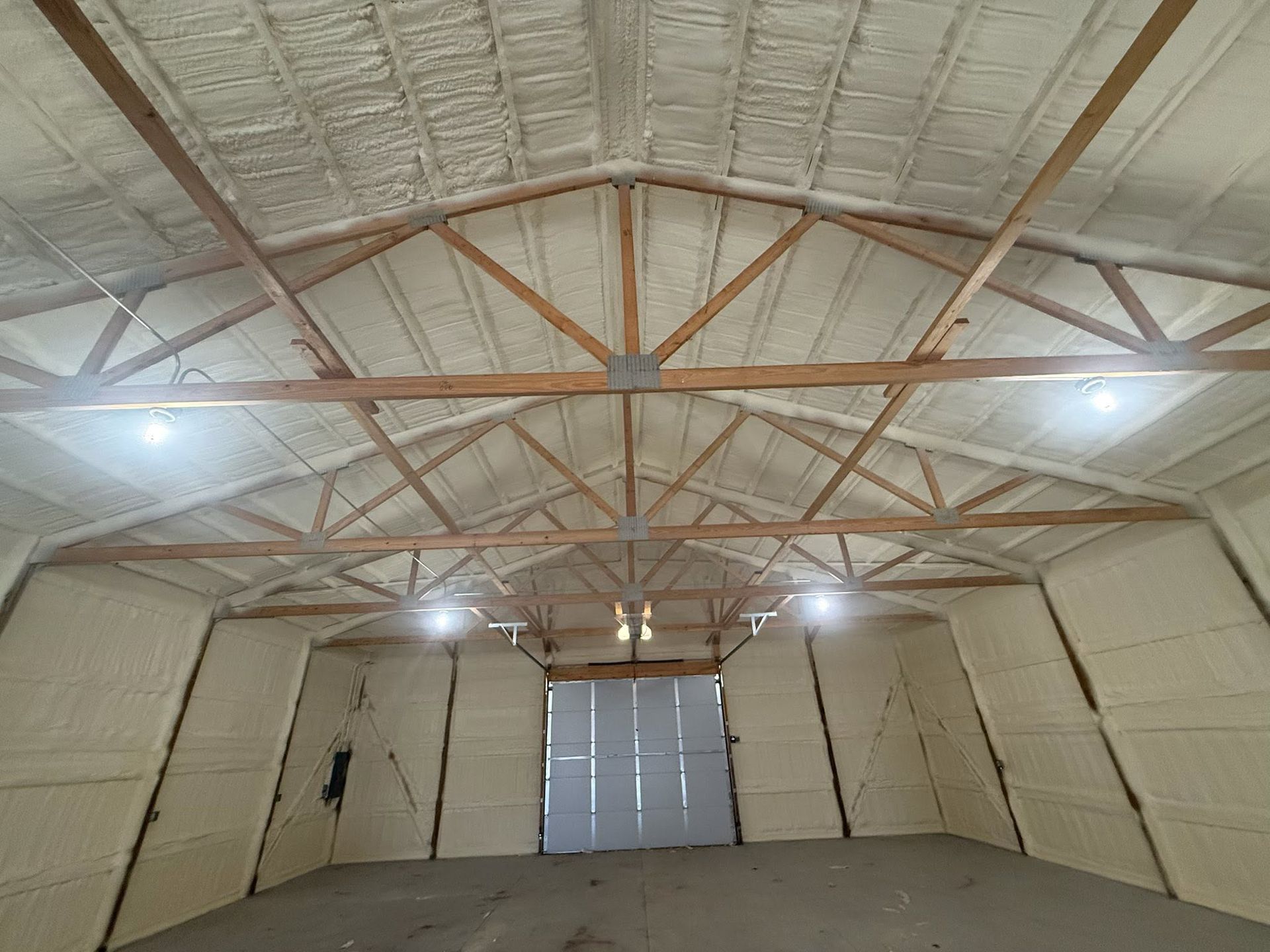 Empty warehouse with insulated walls, exposed wooden trusses, and a closed roll-up door.