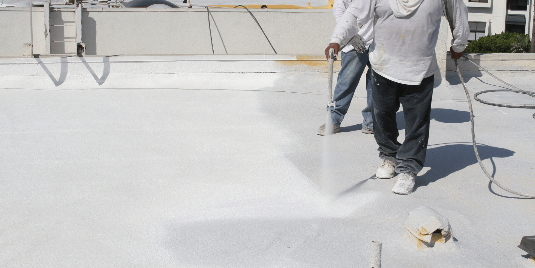 Workers spray-coating a bright white flat rooftop with hoses and spray equipment
