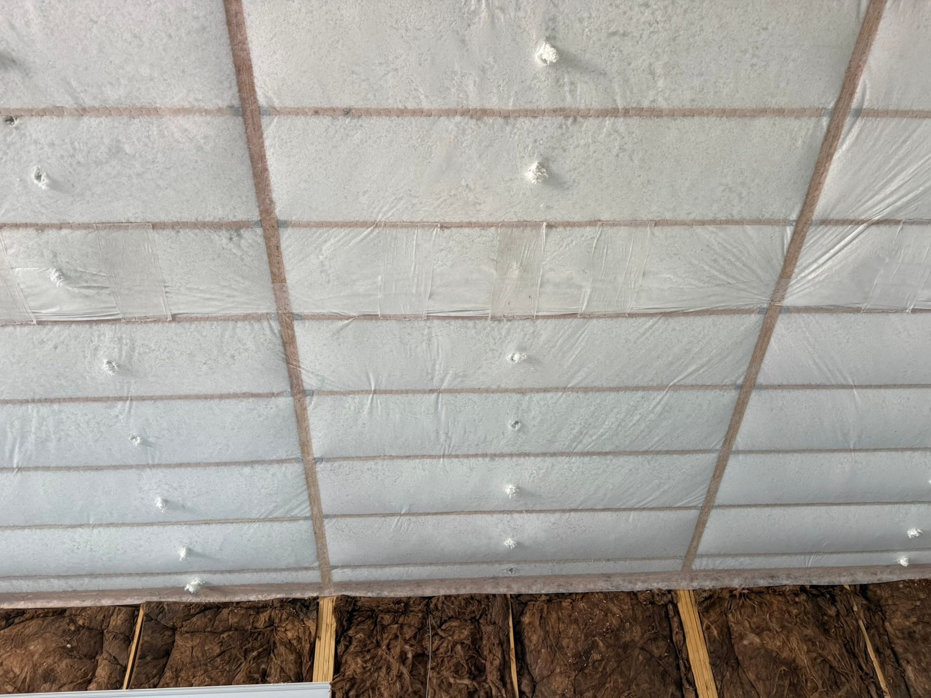 White insulated ceiling with wooden beams and a rough brown wall below.