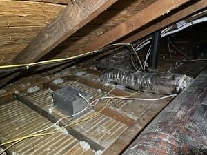 Attic with exposed insulation, wooden beams, and electrical wiring under the roof deck