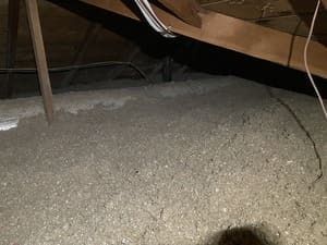 Attic floor covered with loose insulation and exposed wooden beams