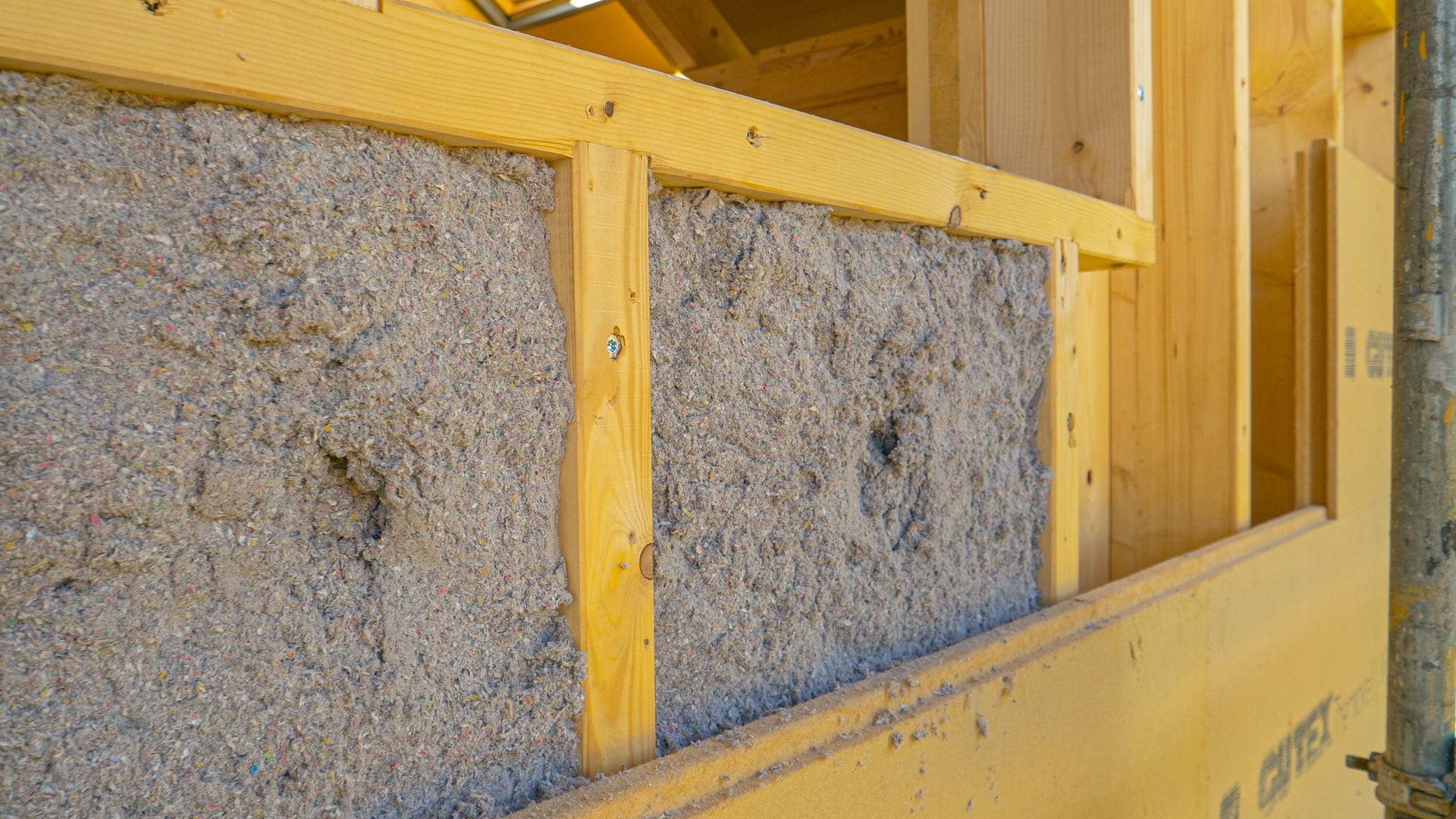 Insulated wooden wall framing with gray fiberglass batts inside an unfinished building.
