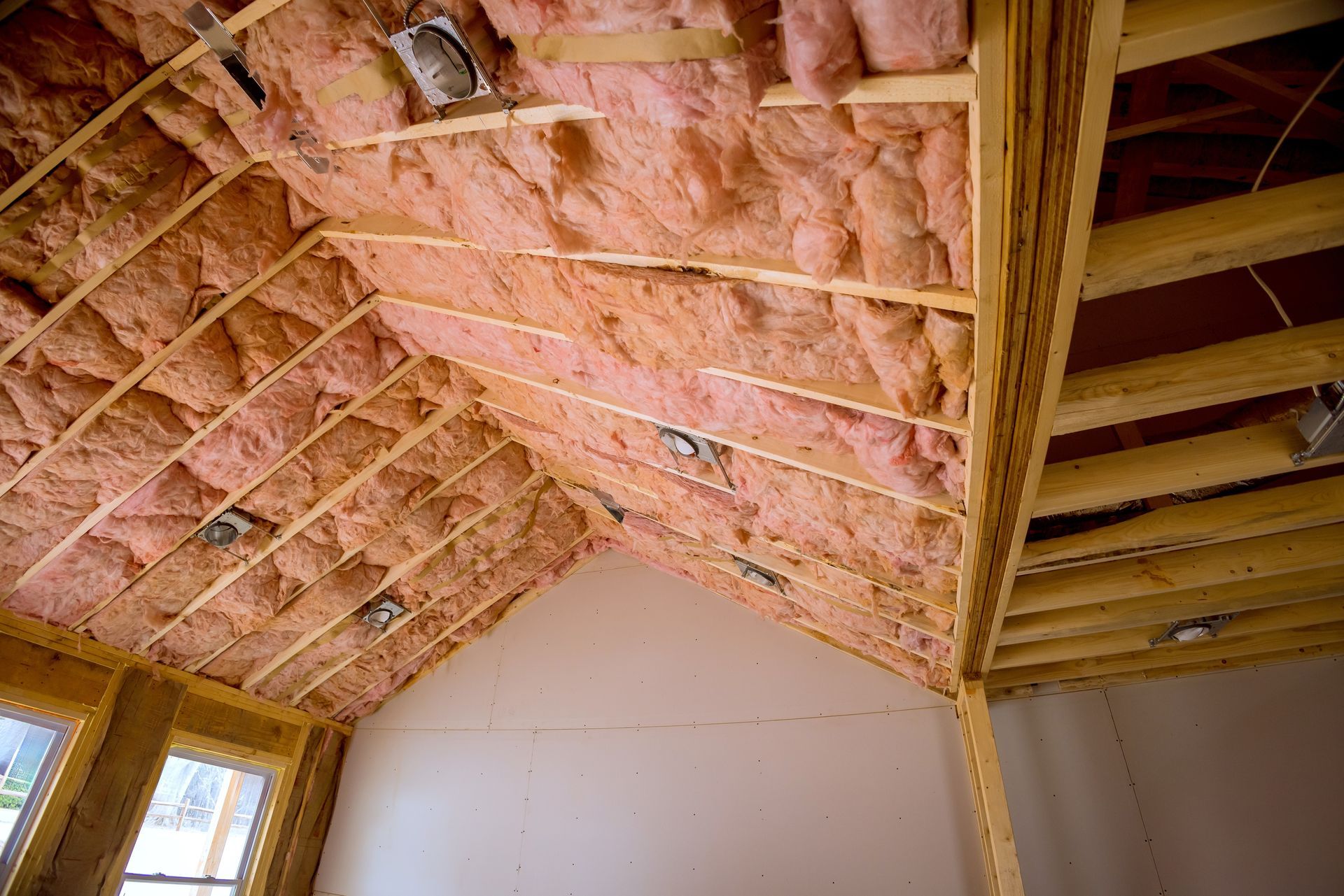 Interior attic with pink insulation between rafters and exposed wooden beams, partially finished walls