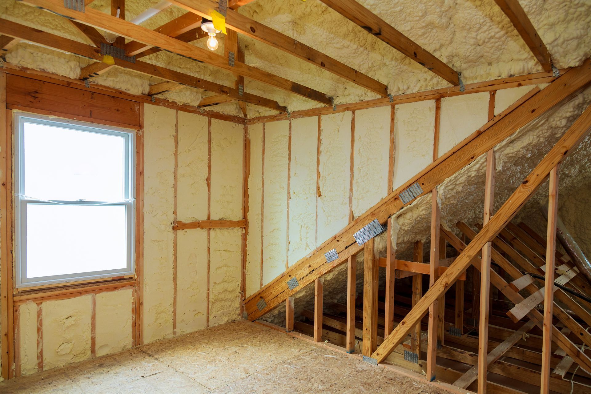 Unfinished room with exposed wood framing, insulation, a window, and staircase framing on the right.