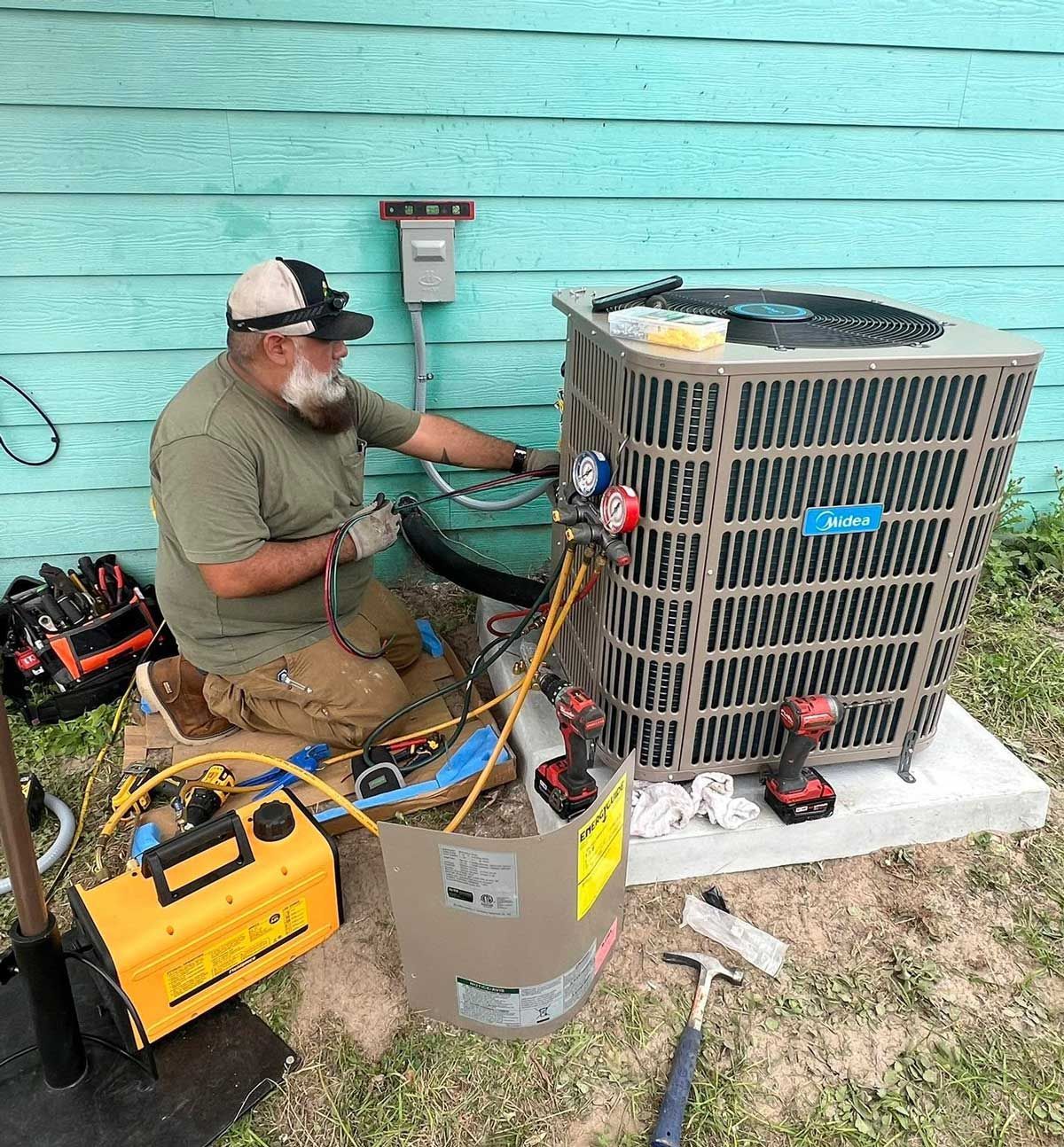 Technician servicing an outdoor air conditioner unit with hoses and tools beside a teal wall. Technician servicing an outdoor air conditioner unit with hoses and tools beside a teal wall.