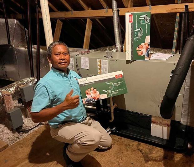 Man kneeling by HVAC ductwork in a crawl space, holding up green product boxes. Man kneeling by HVAC ductwork in a crawl space, holding up green product boxes.