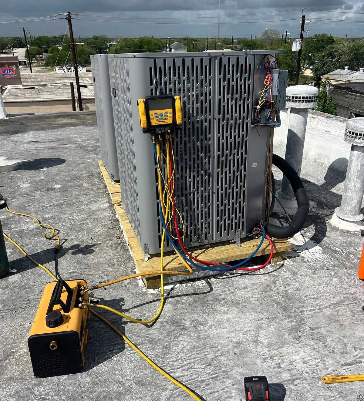 Roof HVAC unit with gauges, cables, and a portable tool on a flat rooftop under cloudy skies Roof HVAC unit with gauges, cables, and a portable tool on a flat rooftop under cloudy skies