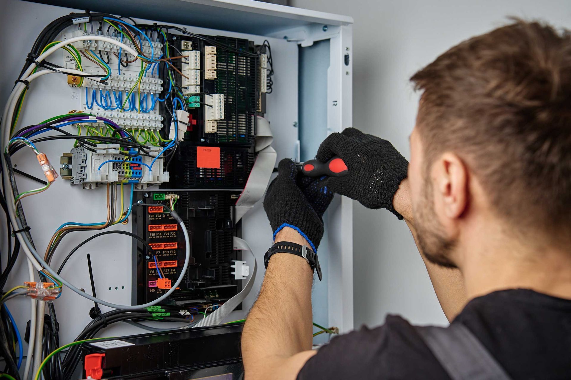 Technician wiring an electrical control panel with a screwdriver inside an open cabinet Technician wiring an electrical control panel with a screwdriver inside an open cabinet