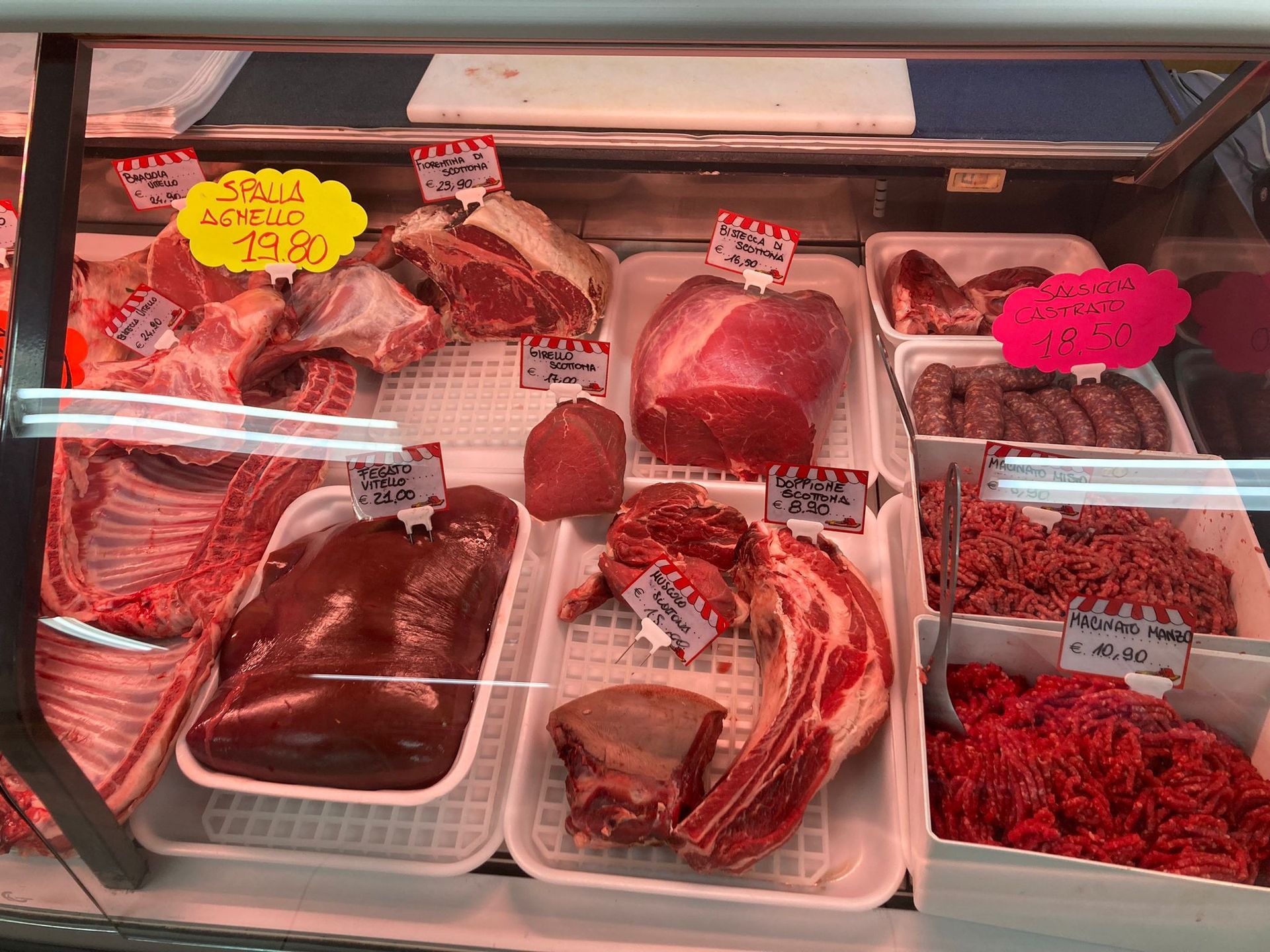 Una vetrina refrigerata per la carne, piena di vari tagli di manzo crudo, frattaglie e salsicce, ognuno con il proprio cartellino del prezzo.