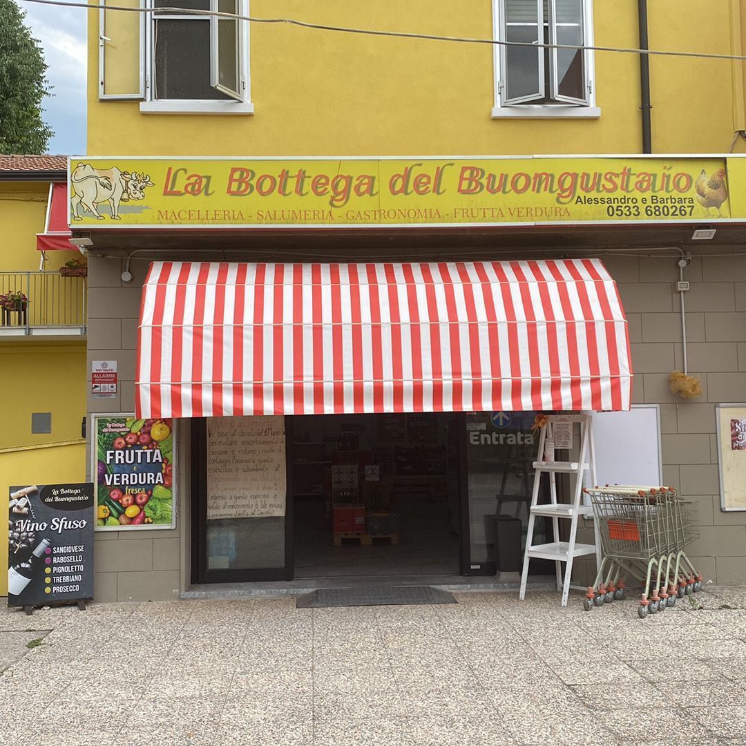 Vetrina del negozio La Bottega del Buongustaio con tenda a strisce rosse e bianche, lavagna con il menù e carrello della spesa all'esterno.