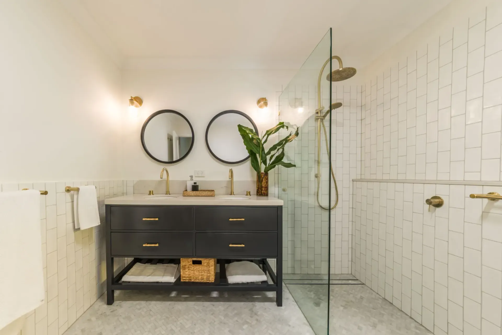Modern bathroom with black vanity, round mirrors, glass shower, and white tiled walls
