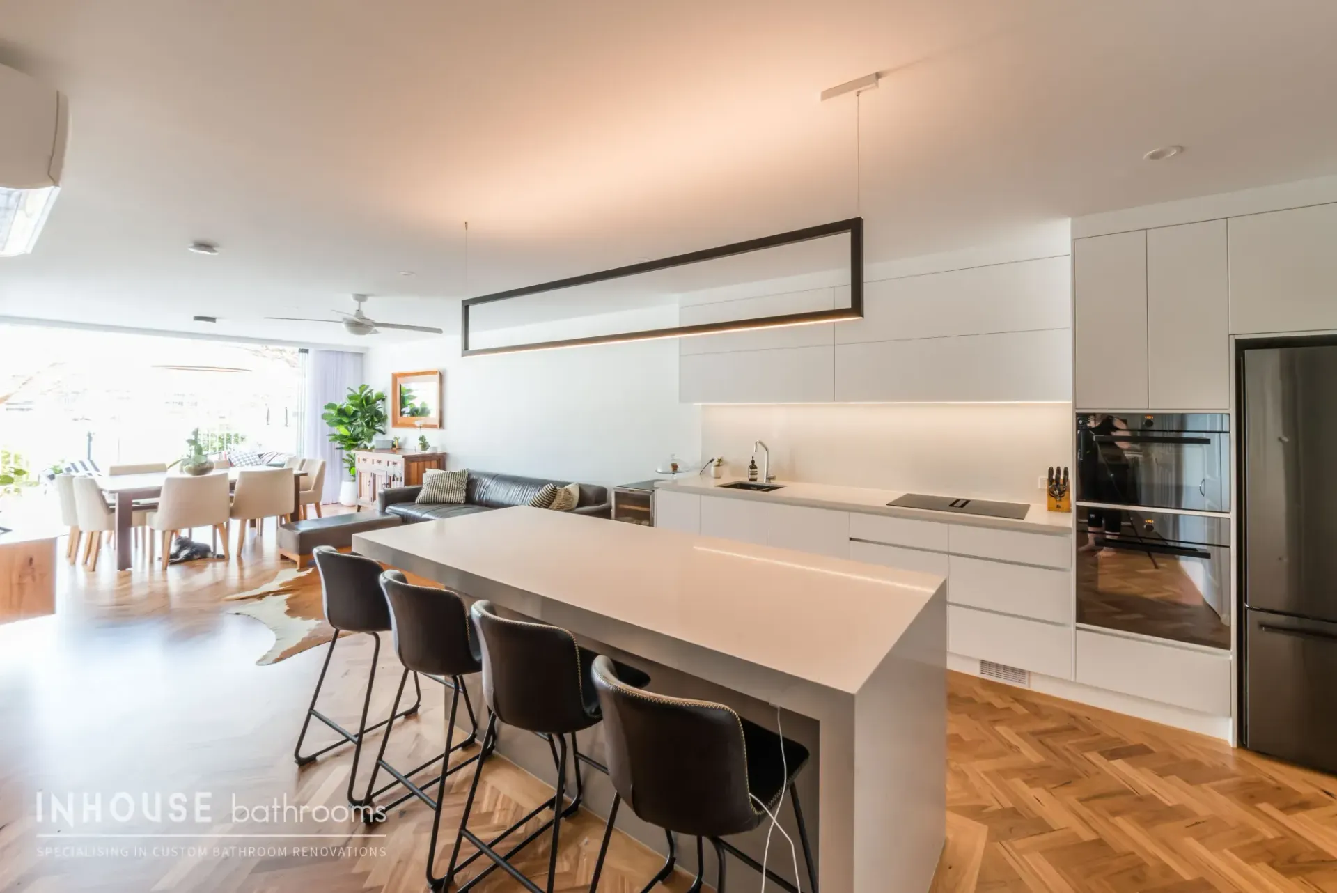 Modern open-plan kitchen with large island, black stools, white cabinetry, and wood floors