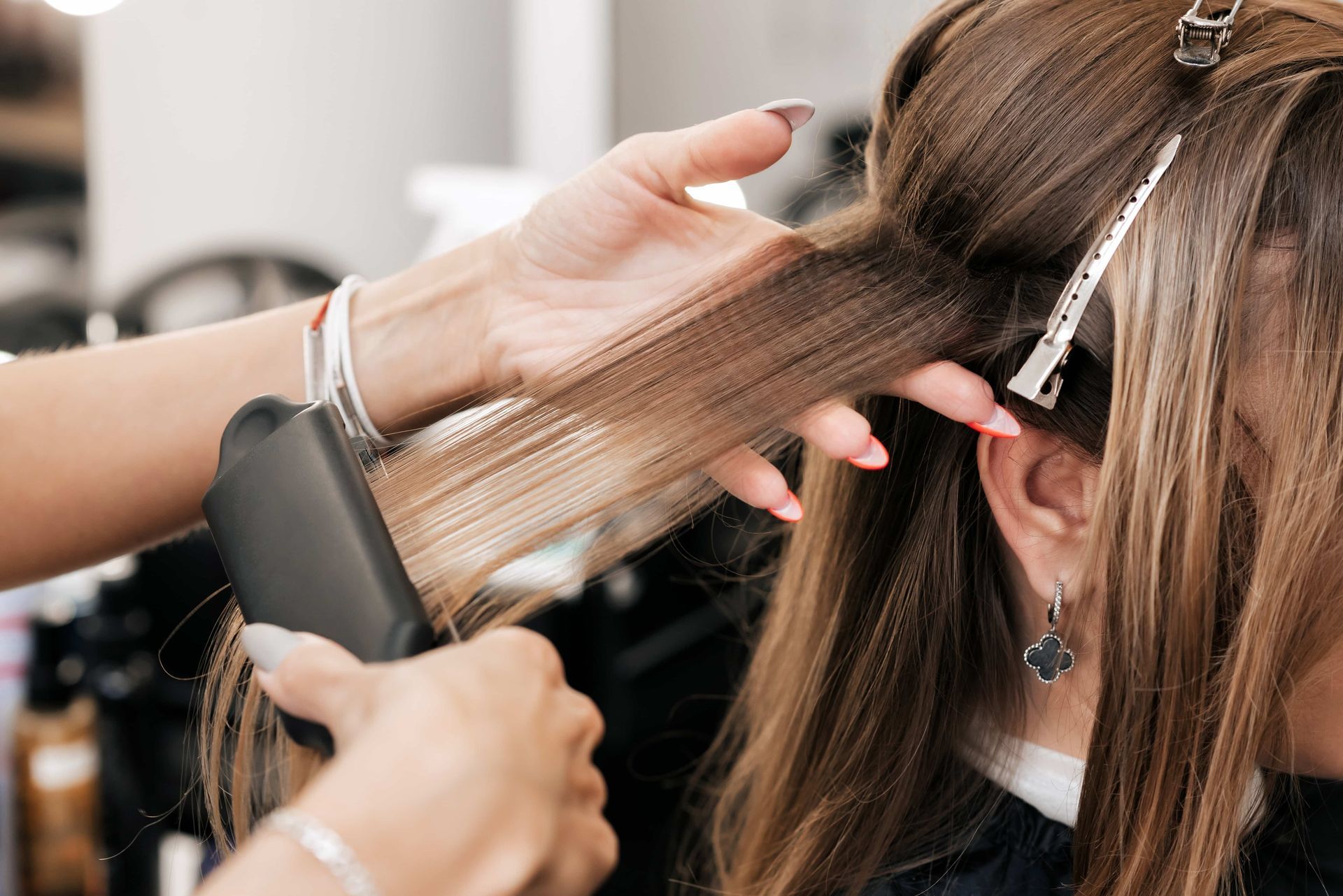 Hands using a flat iron on brown hair in a salon.