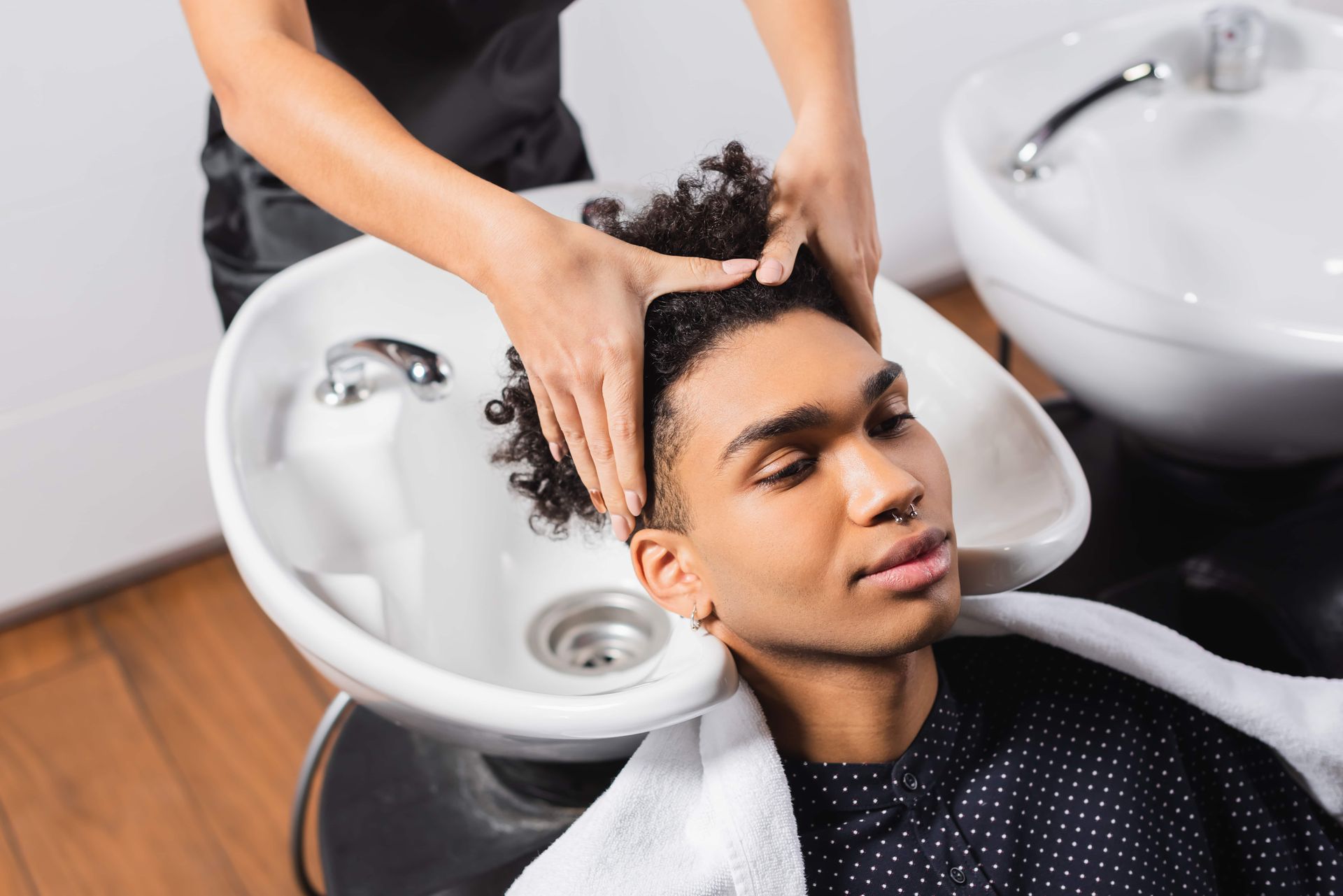 A person having their hair washed at a salon, head over a sink, with hands gently massaging their head.