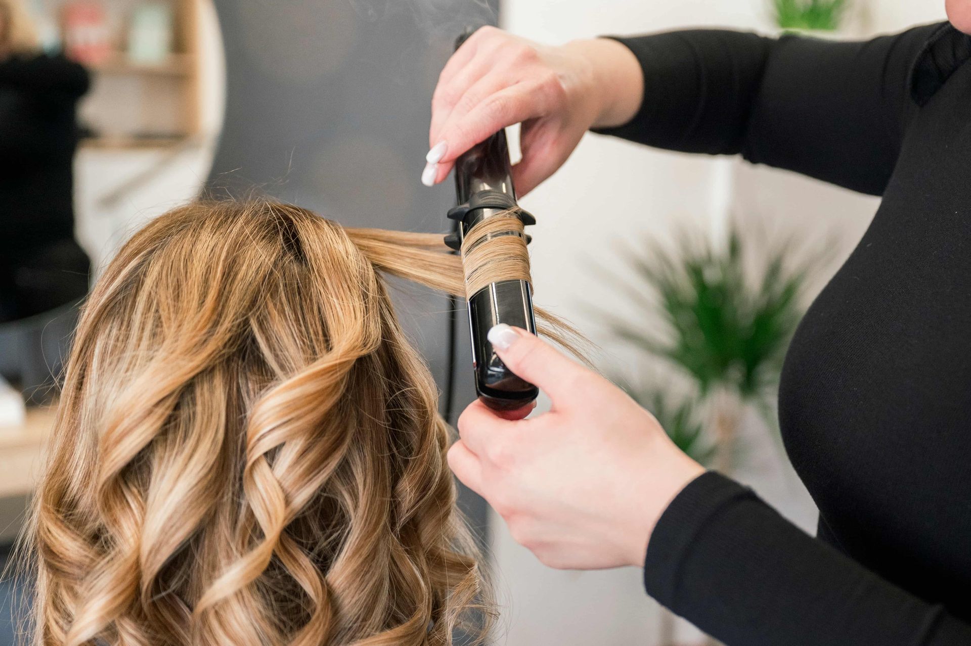 Person curling hair with a curling iron in a salon.