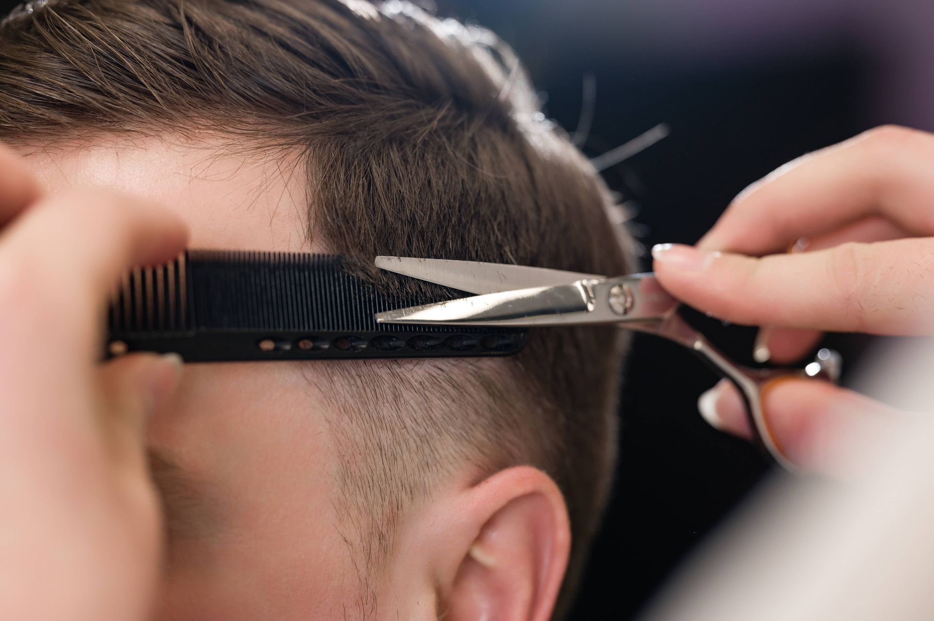Hair stylist trimming client's hair with scissors and comb in a salon setting.
