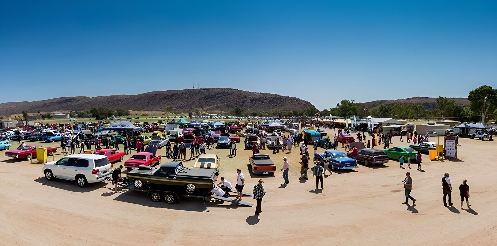 Busy Outdoor Market with Many People, Colorful Vehicles, and Tents in A Dusty Open Area Beneath a Low Hill — Blatherskite Park in Ilparpa, NT