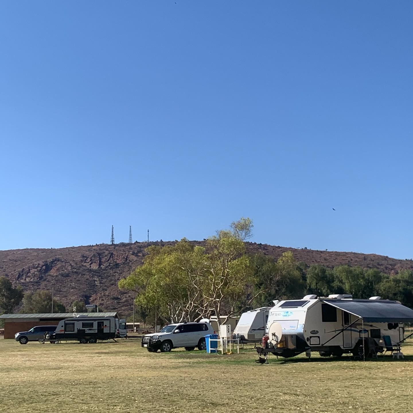 Campground with R vs And Trucks on Grassy Land Beneath a Rocky Hill Under a Clear Blue Sky — Blatherskite Park in Ilparpa, NT