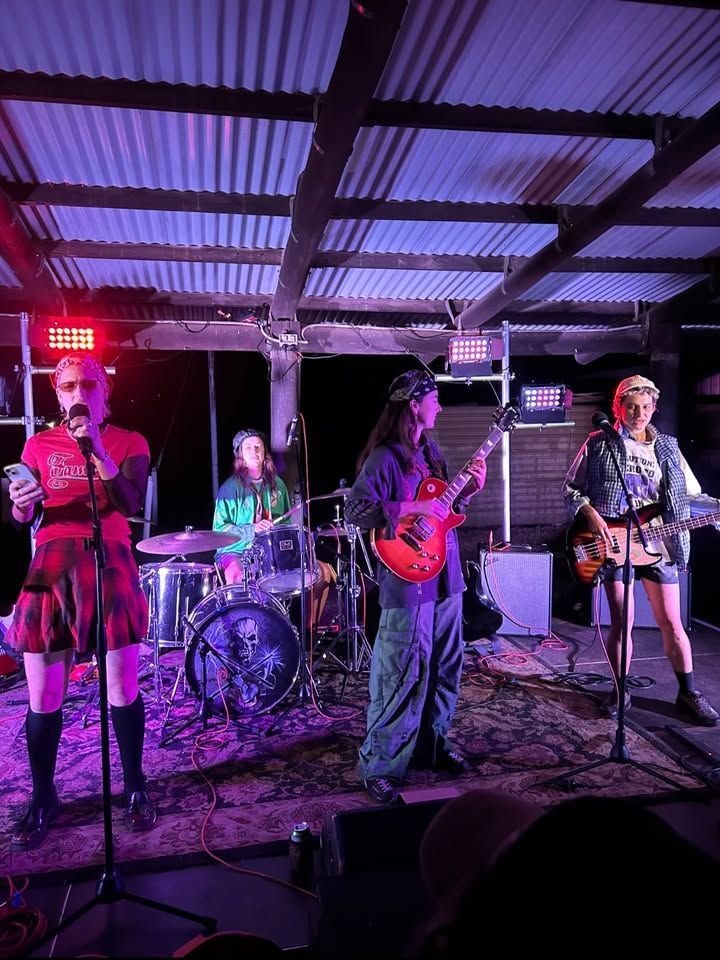 Four Person Band Performing on A Lit Outdoor Stage, with Drums, Guitars, and Microphone Stands — Blatherskite Park in Ilparpa, NT