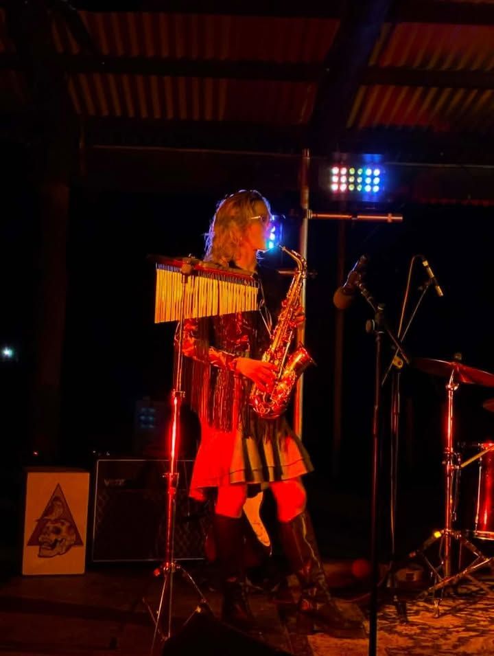 Musician in Red Lit Stage Performing Saxophone Beside Drum Kit and Microphone Stands — Blatherskite Park in Ilparpa, NT