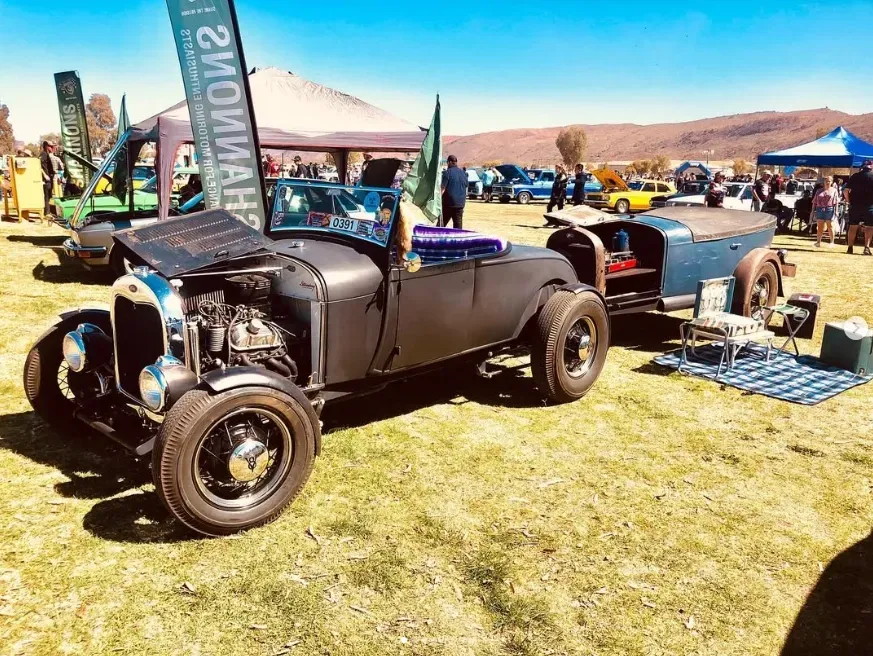Black vintage hot rod on grass at an outdoor car show with tents and mountains in the background — Blatherskite Park in Ilparpa, NT