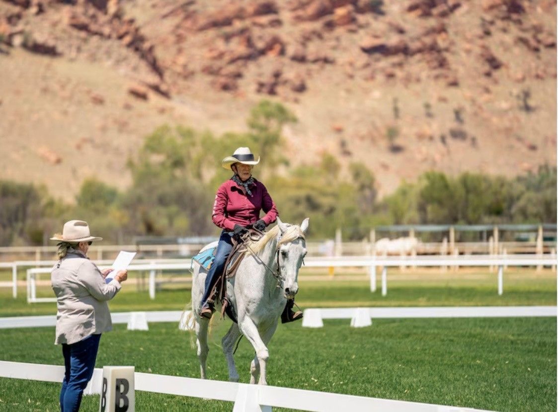 Person Riding a Horse While Another Person Stands Nearby at An Outdoor Arena with Desert Hills — Blatherskite Park in Ilparpa, NT