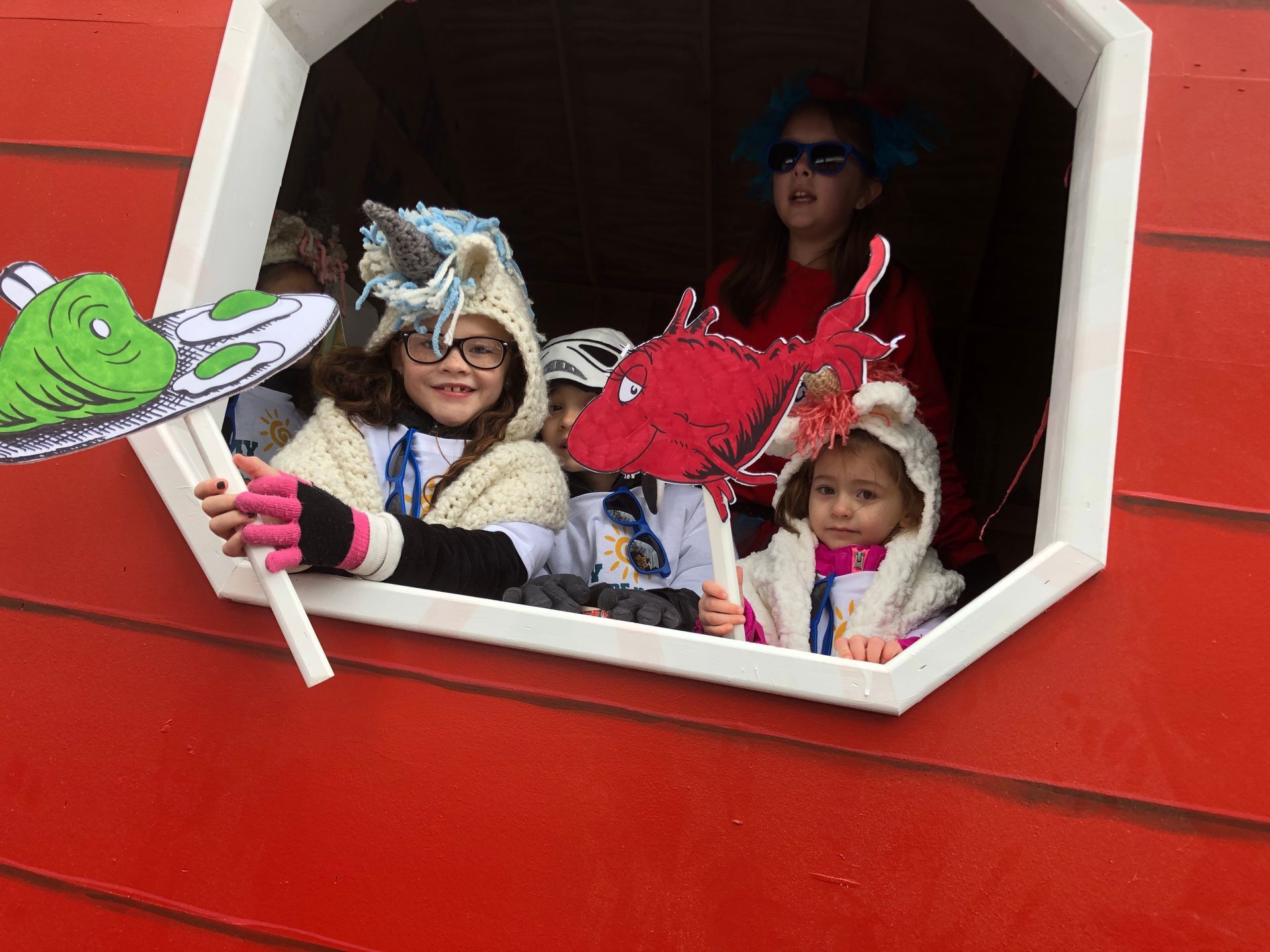 Children in costumes inside a red structure; one holds a green creature, another a red fish.