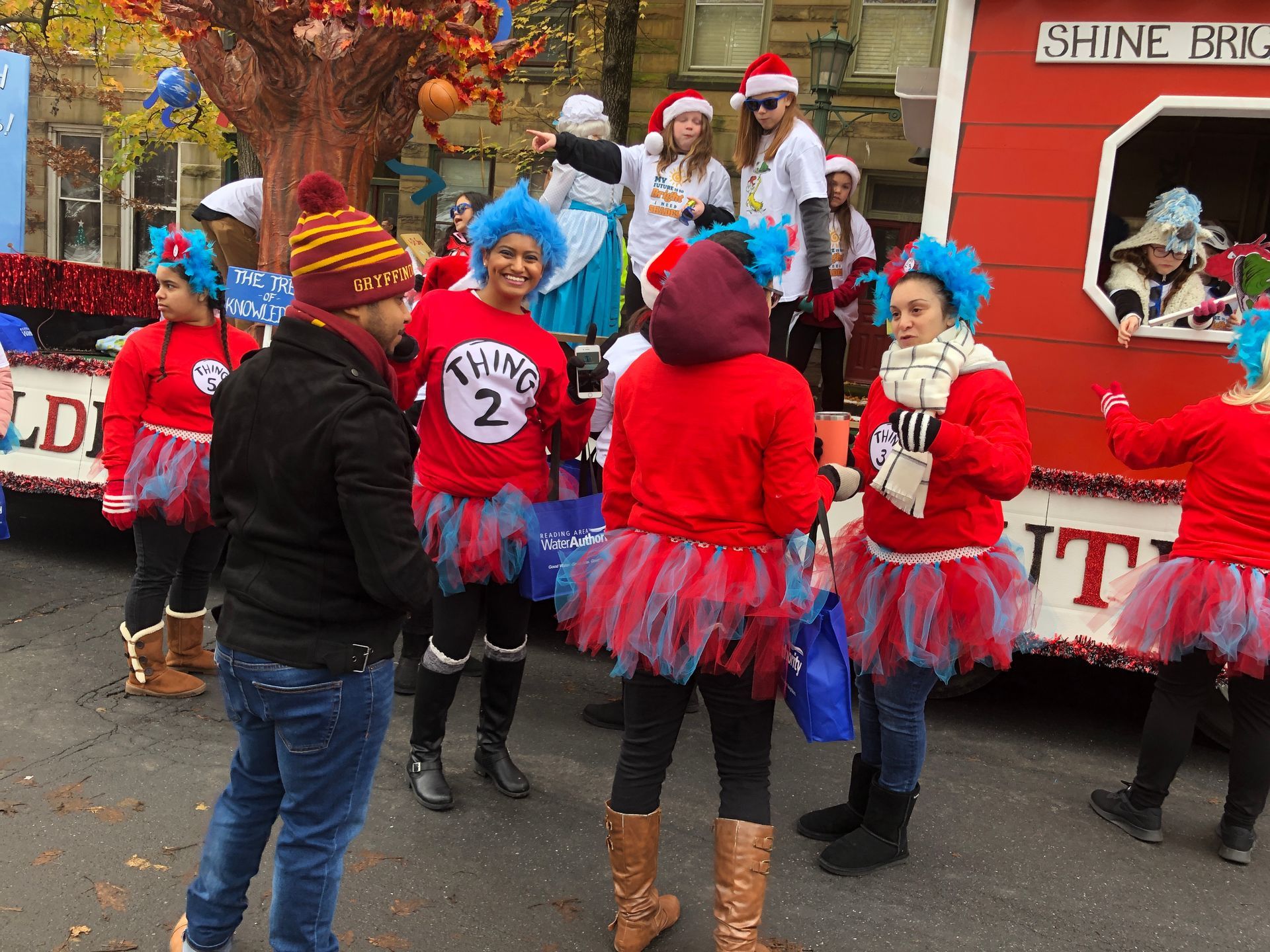 People in red sweaters, tutus, and blue wigs, Thing 1 & 2 themed, on a parade float with Christmas decorations.