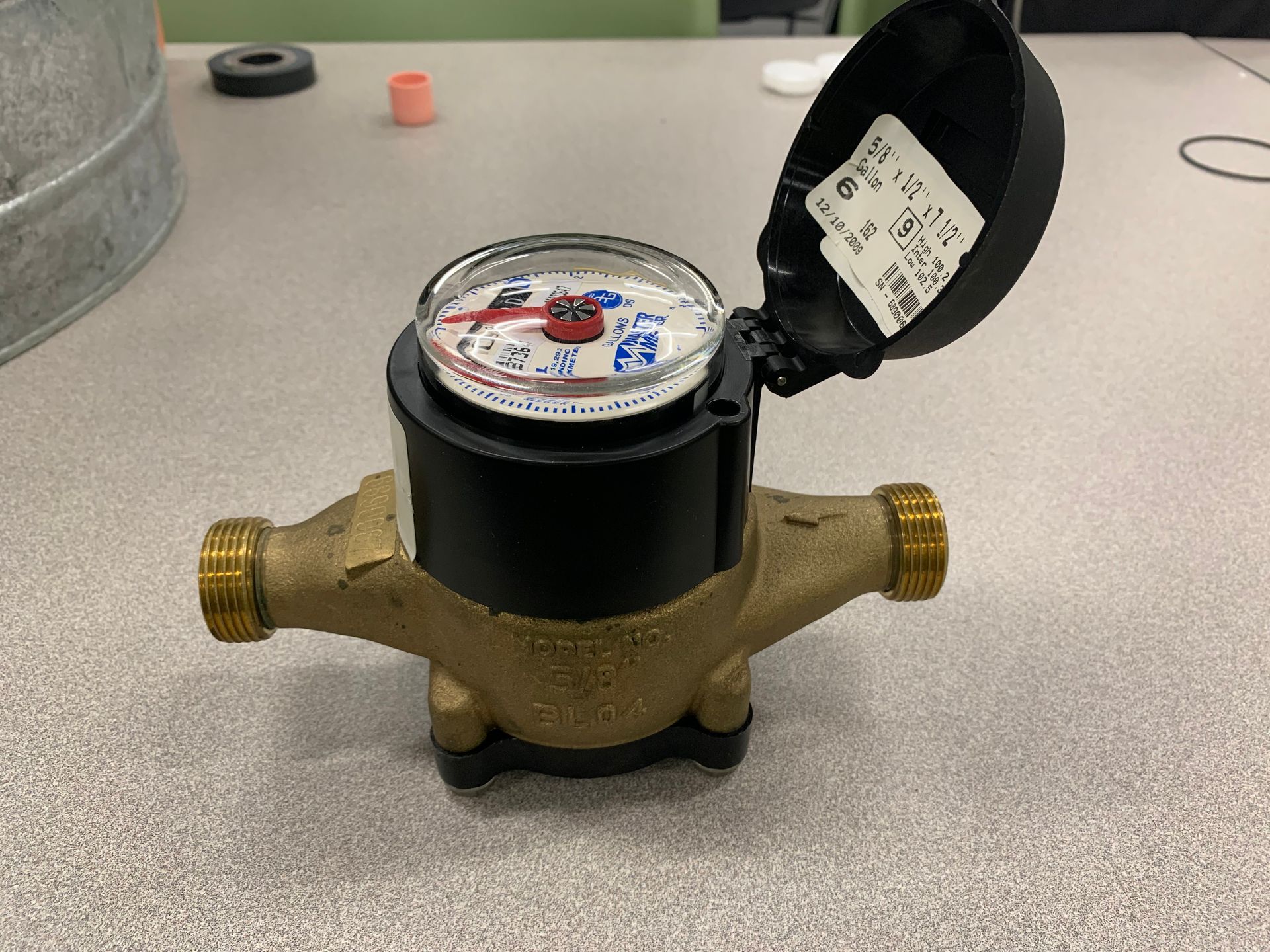 Water meter with a brass body and a black top, cover open, displaying the dial.