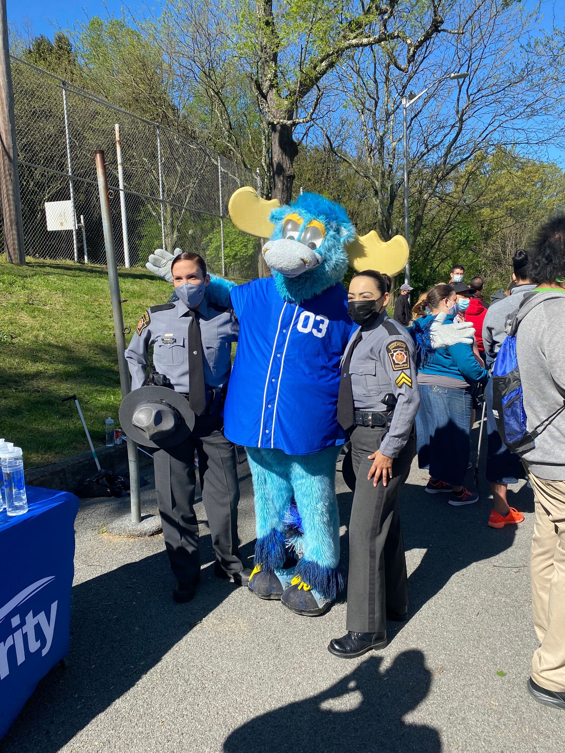 Two police officers and a blue moose mascot stand outside on a sunny day.