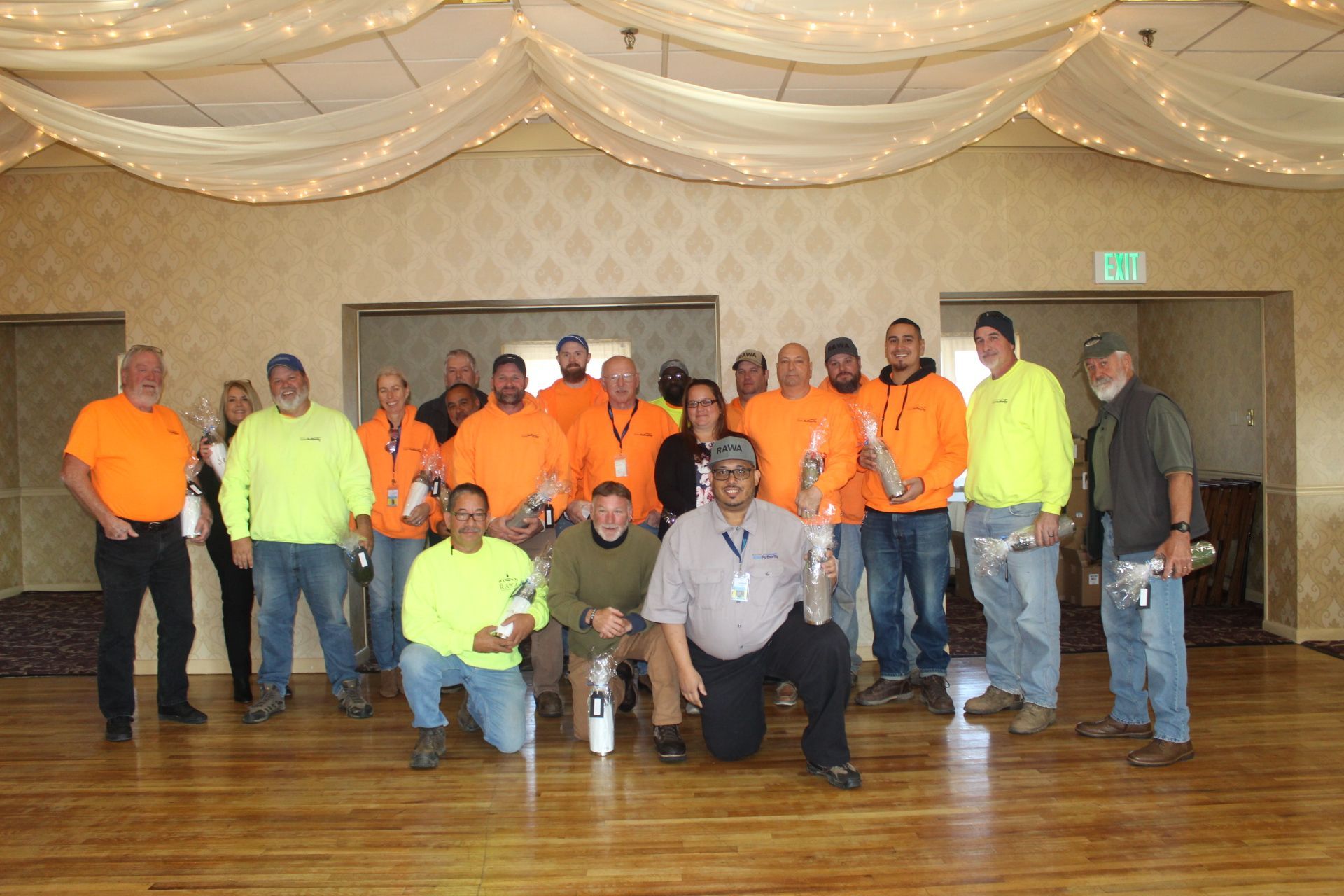 Group of people in bright safety vests and orange shirts holding trophies in a ballroom.