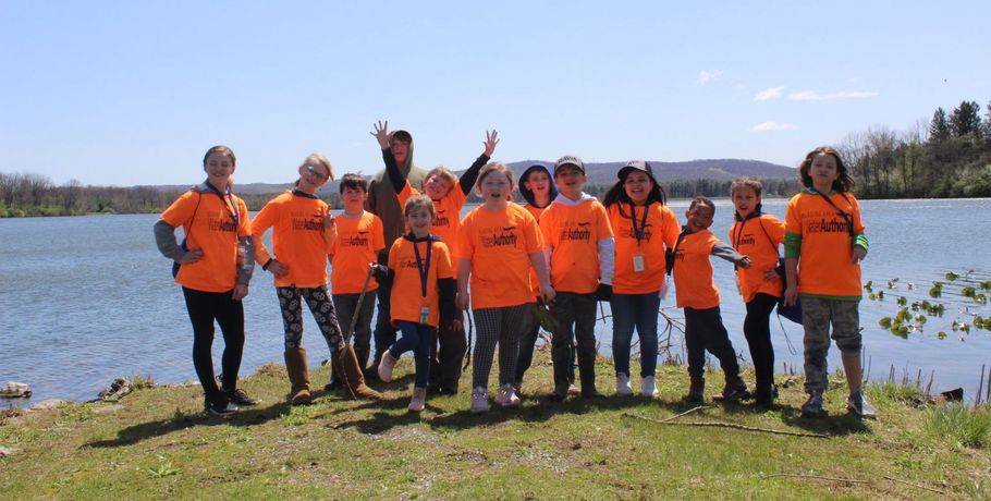 Group of people in orange shirts poses by a lake on a sunny day.