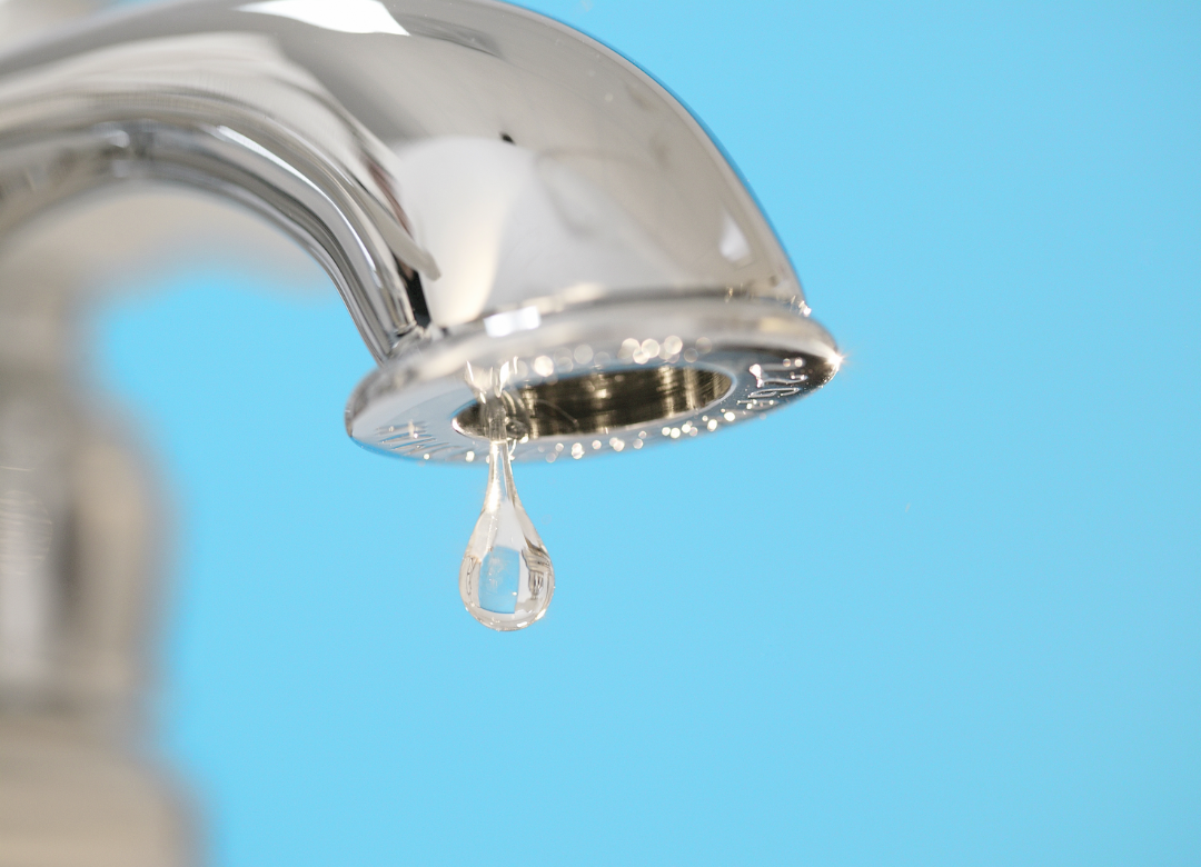 A chrome faucet with a water droplet falling against a blue background.